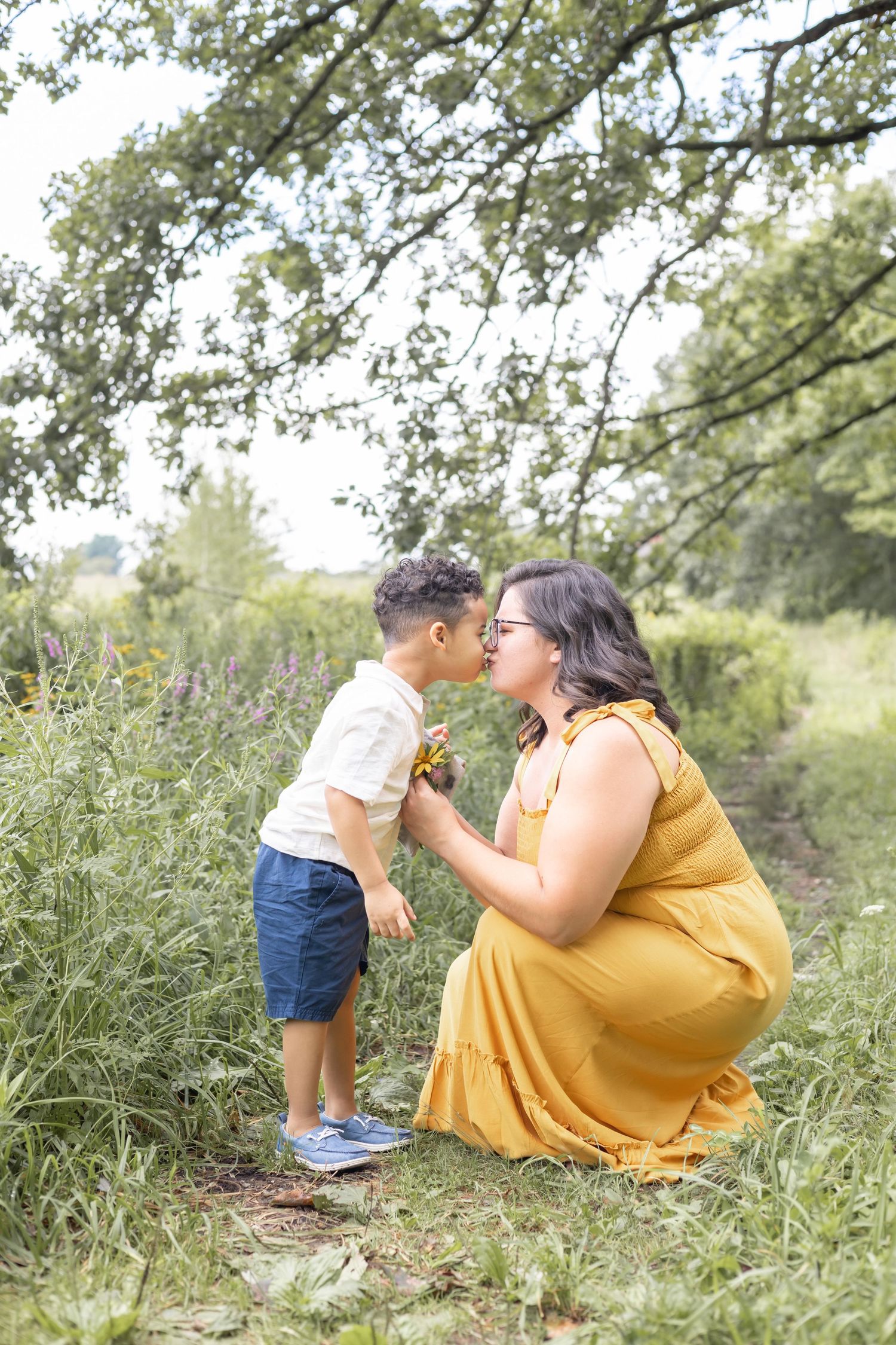 A sweet moment shared between parent and child holding dandelion flowers in a summer meadow beneath flowering trees.