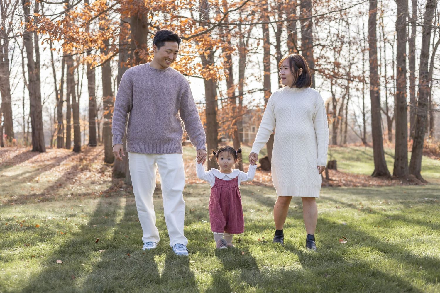 Three people walking together and holding hands in a sunlit autumn forest with dried leaves on the ground.