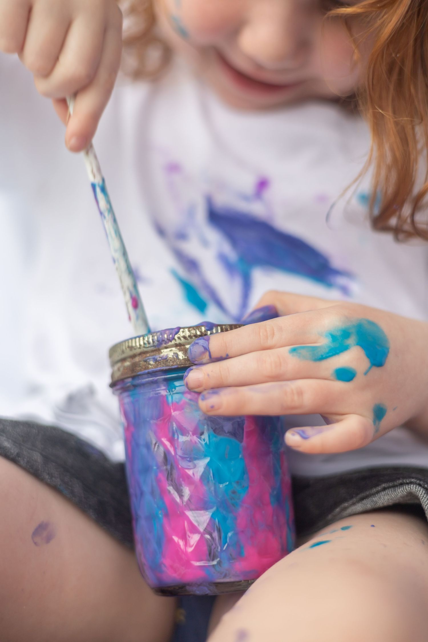Close-up sequence showing hands holding and stirring a glass jar filled with swirling pink and blue watercolors.