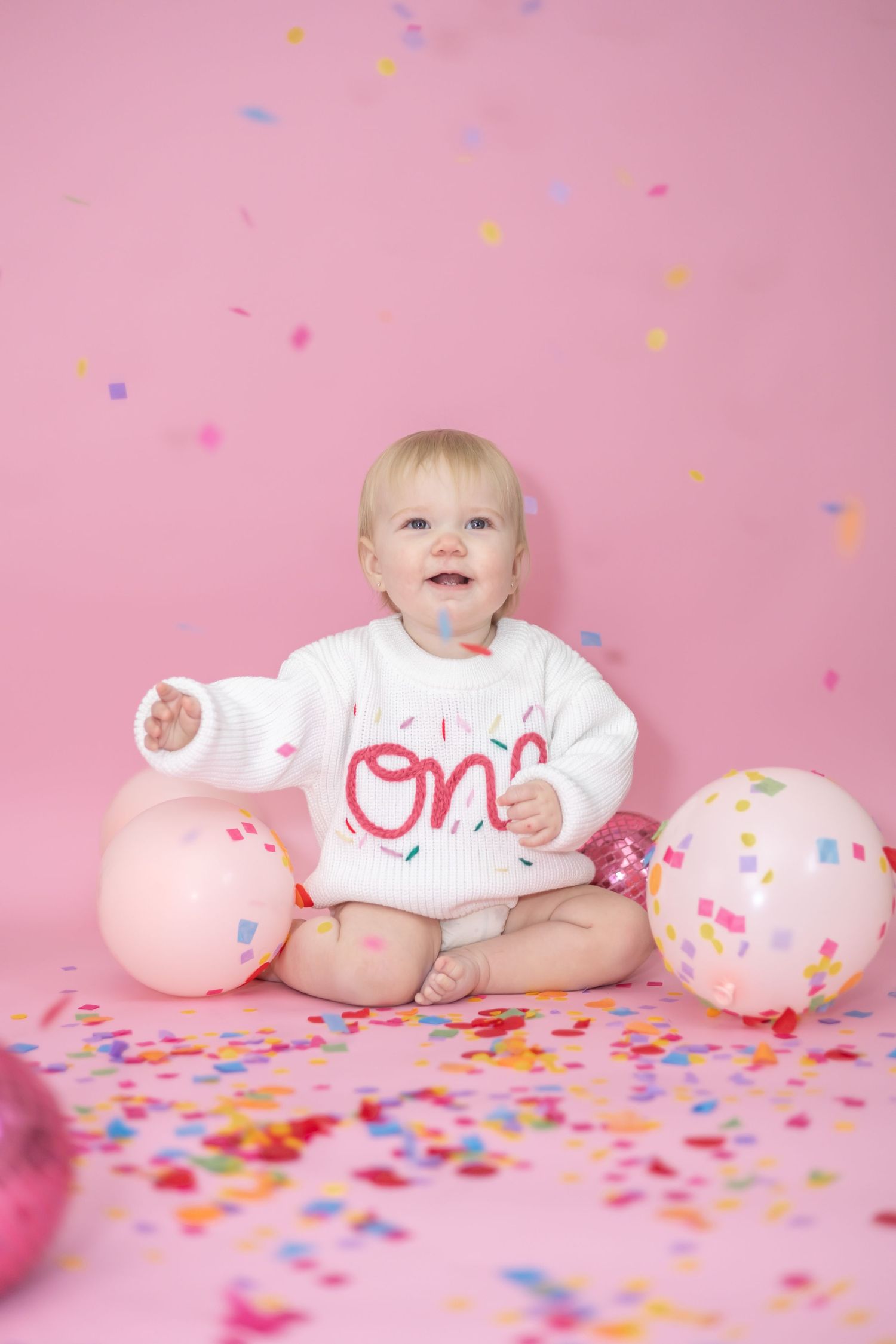 Festive scene with party balloons and colorful confetti on pink backdrop, celebrating a cheerful occasion.