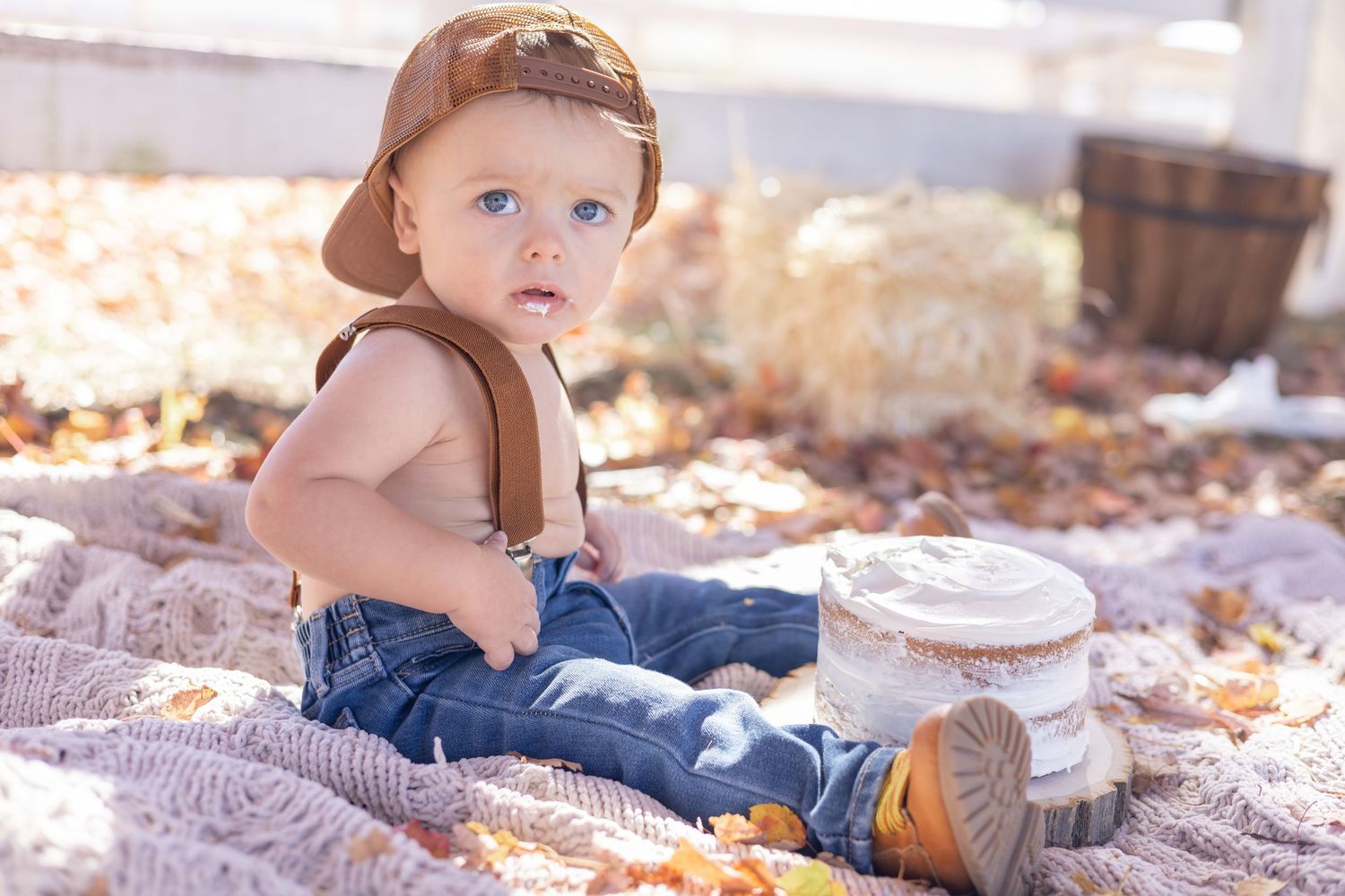 Baby sits on cozy blanket surrounded by fallen leaves and wooden blocks in autumn sunlight.