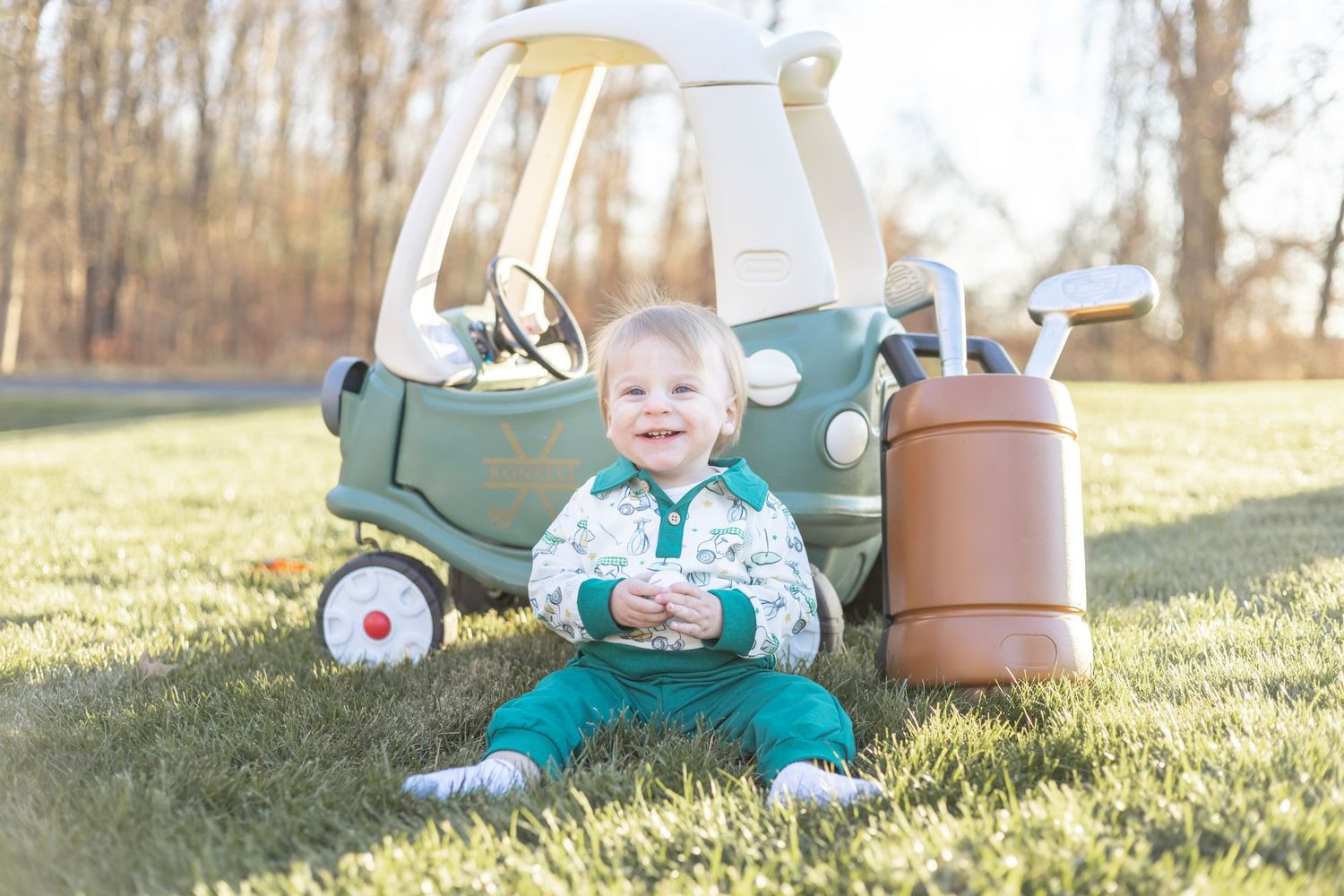 Young child sits in sunlit grass playing with gardening tools and terracotta pots.