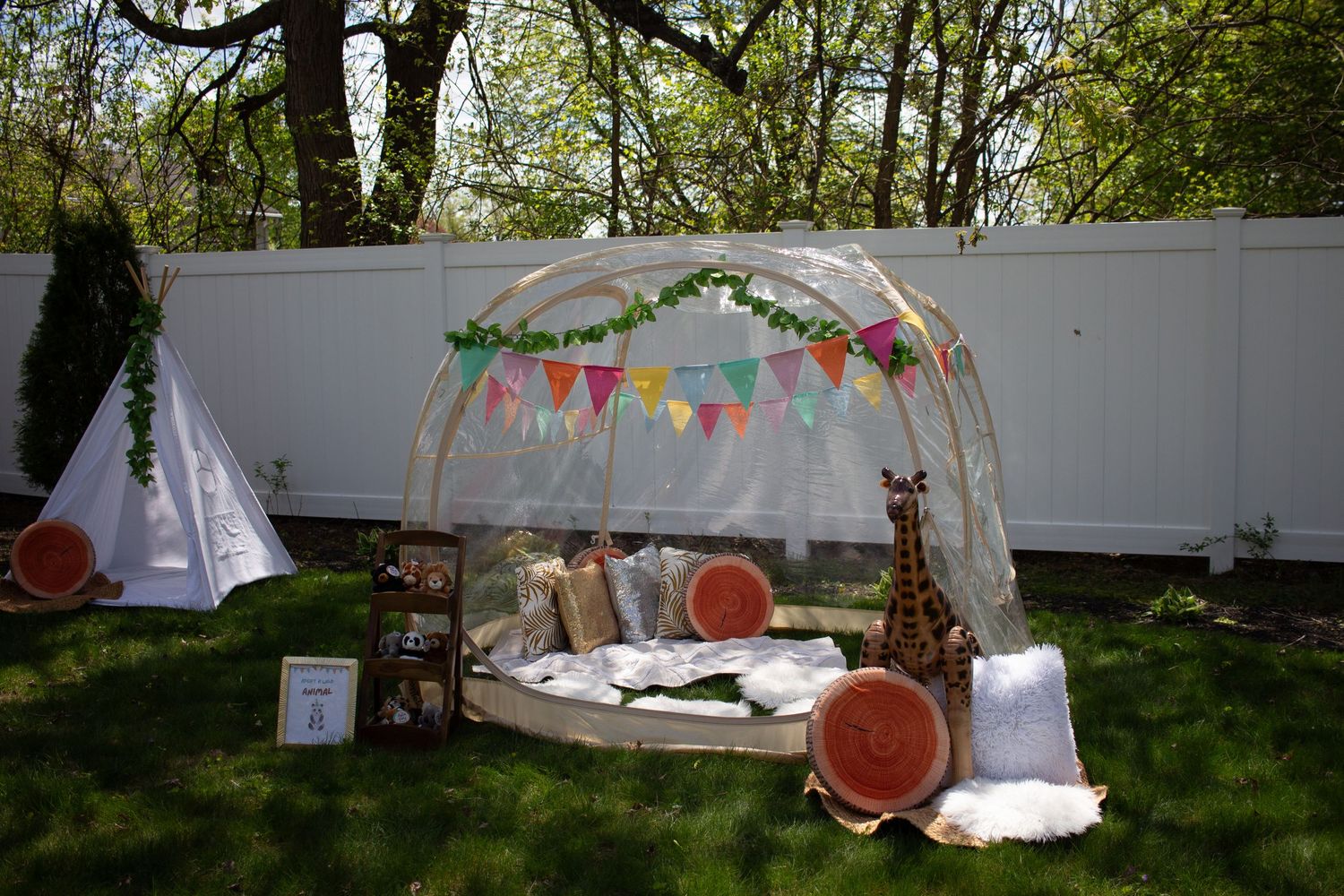 White decorative canopies with bunting and twinkle lights set up in a lush garden setting for an outdoor event.