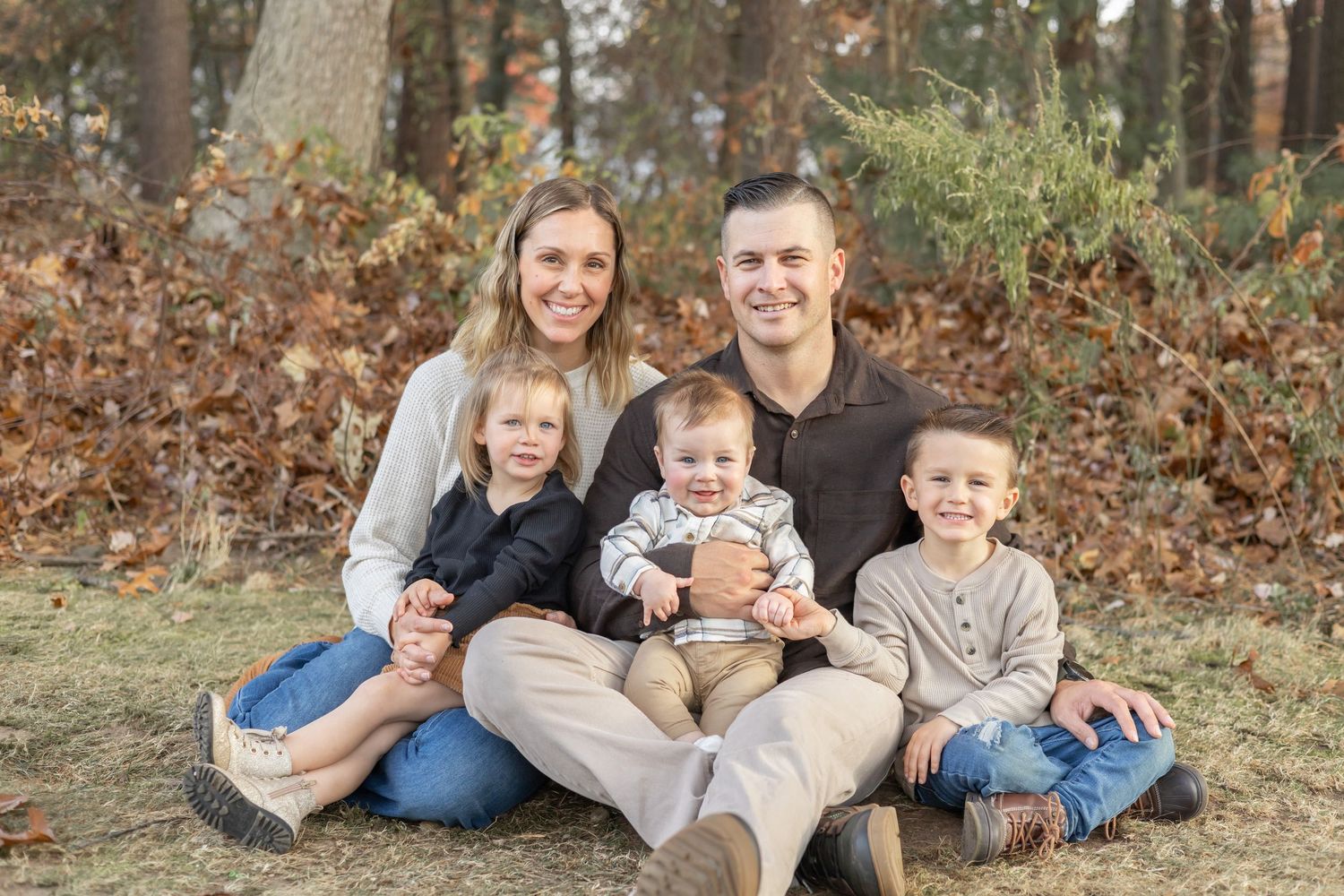 Family portrait with parents and three children sitting together in autumn setting.
