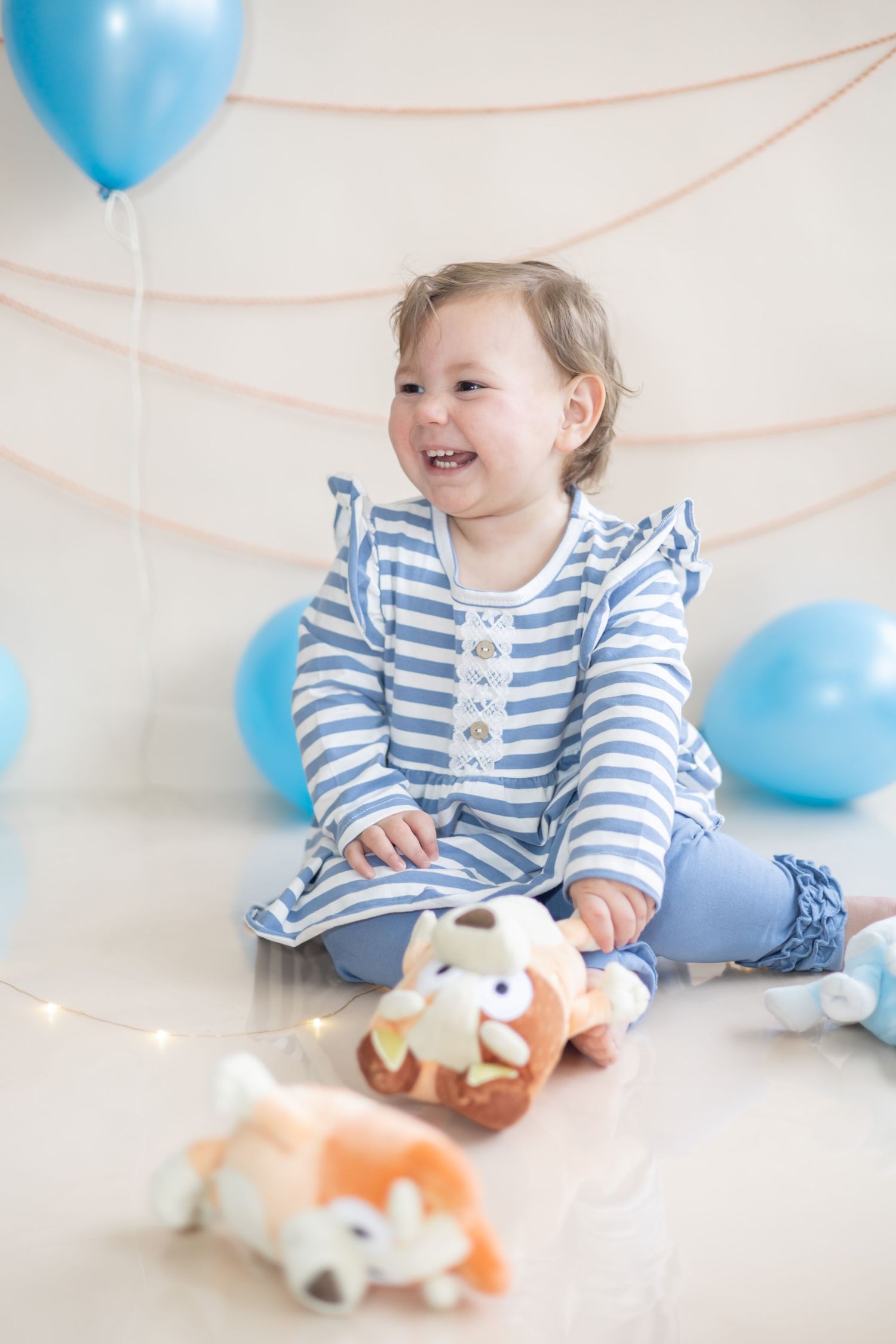 A joyful scene with blue balloons and a striped outfit while playing with a plush toy on white background.