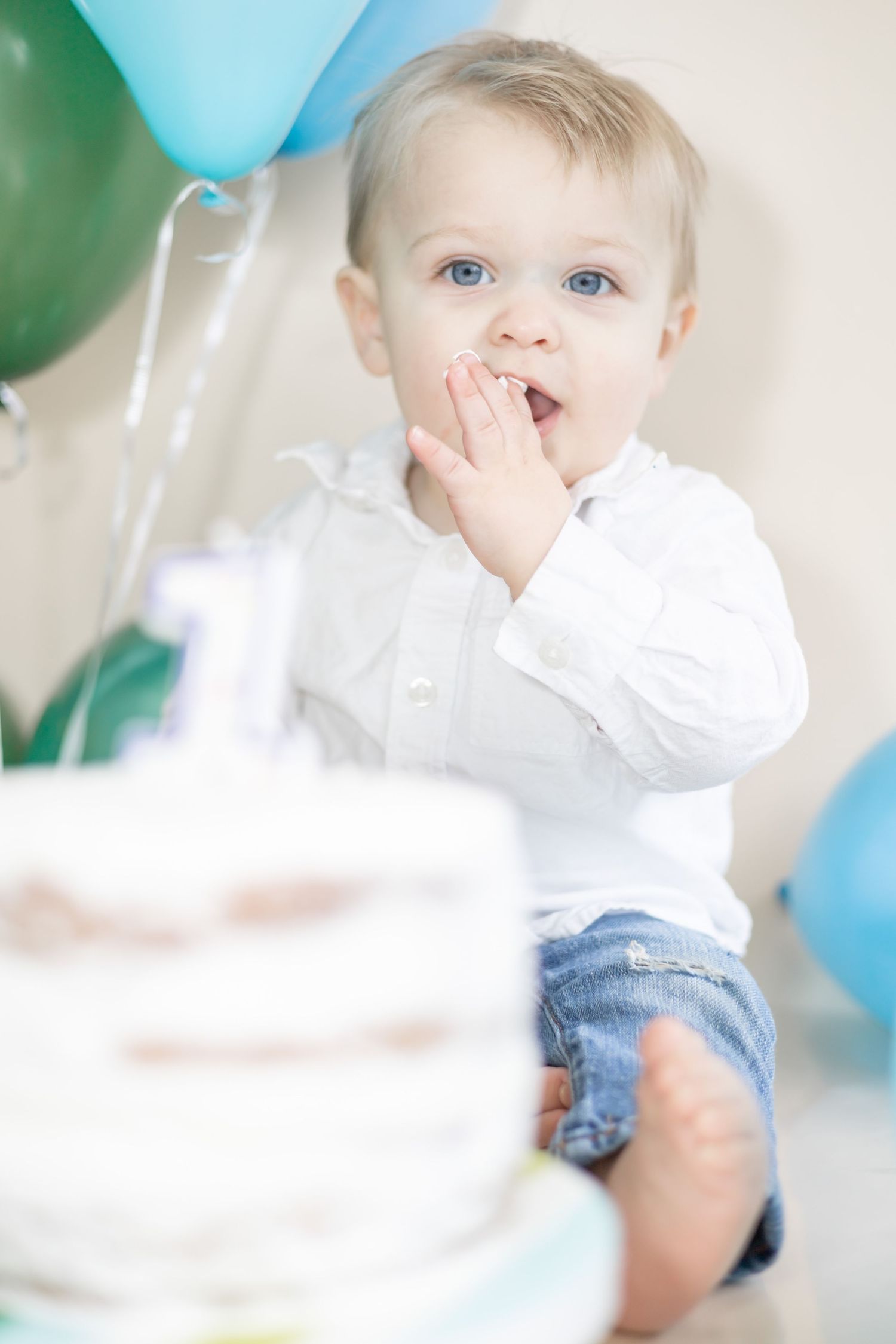 Young child in white shirt and denim with blue and white balloons in soft focus celebration setting.