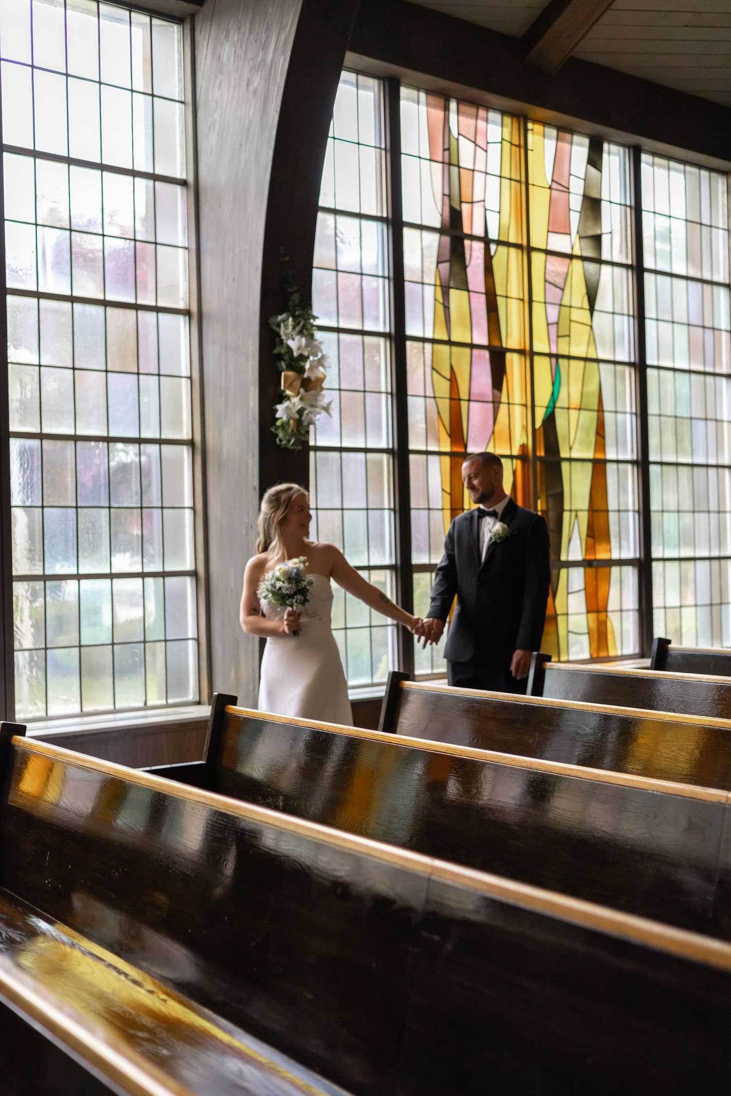 Wedding couple holding hands in a church with beautiful stained glass windows casting colorful light.