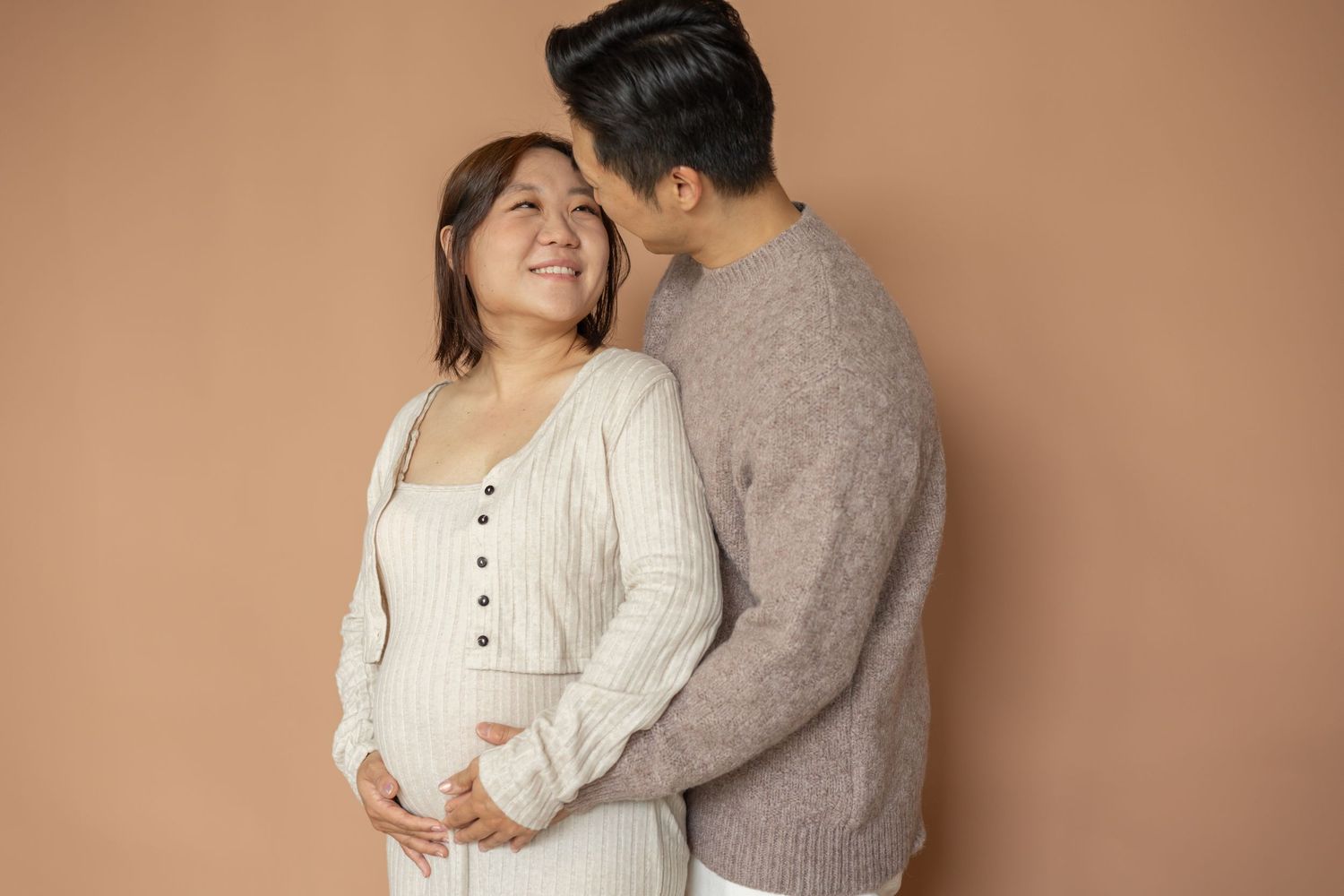 A couple in neutral tones embracing warmly in a romantic photoshoot against a beige background.