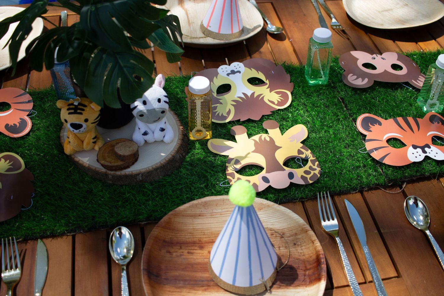 Jungle-themed party table with animal masks on artificial grass and monstera leaves as decorations.