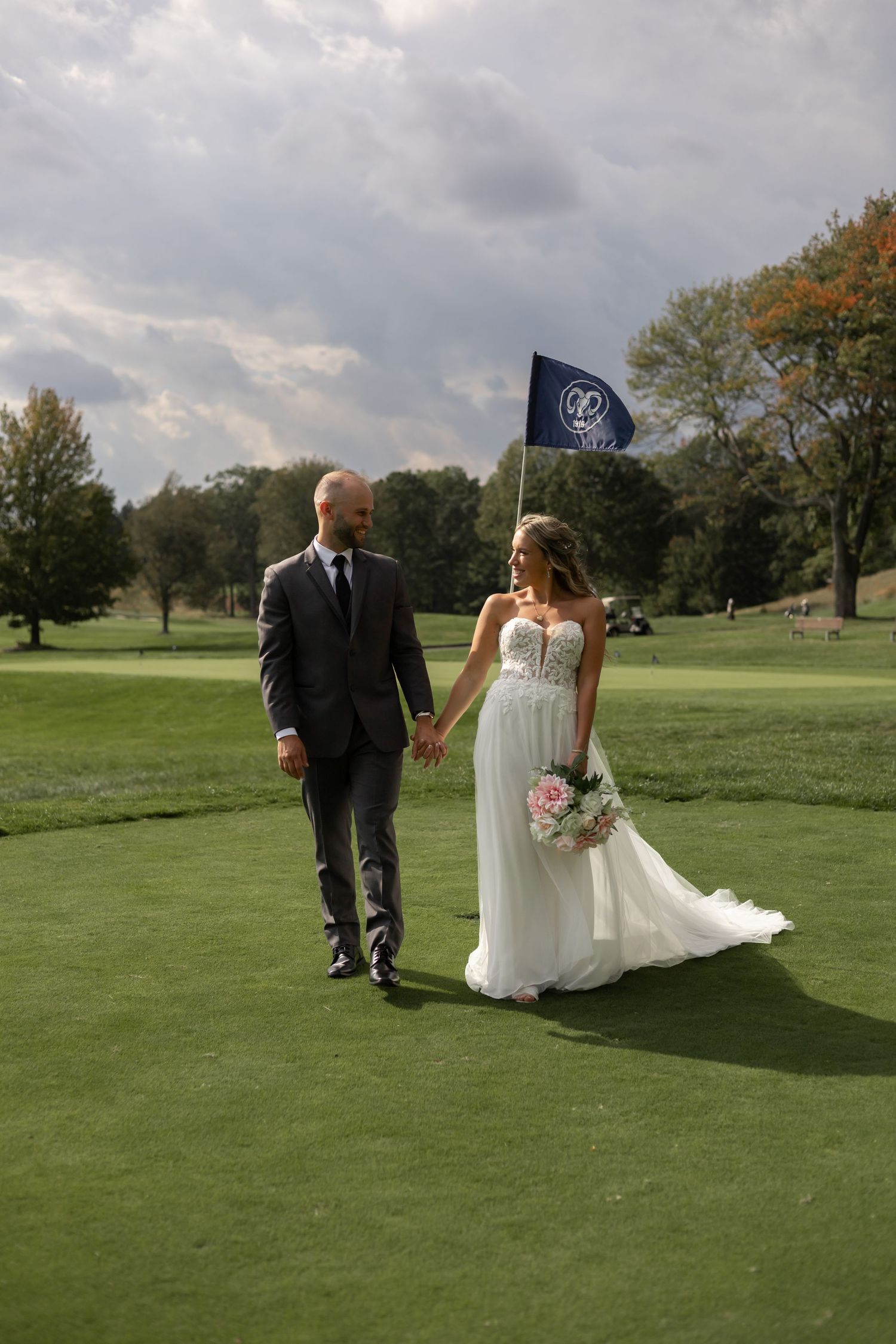 A couple in wedding attire poses for romantic photos on a green golf course under cloudy skies.