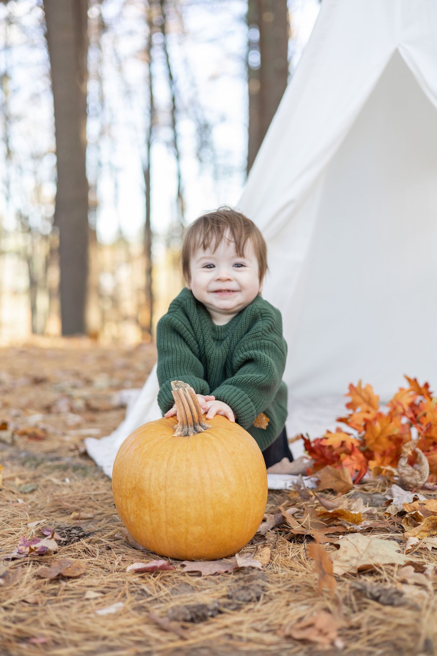 Autumn outdoor photos with pumpkin and fallen leaves near a white teepee tent in the woods.