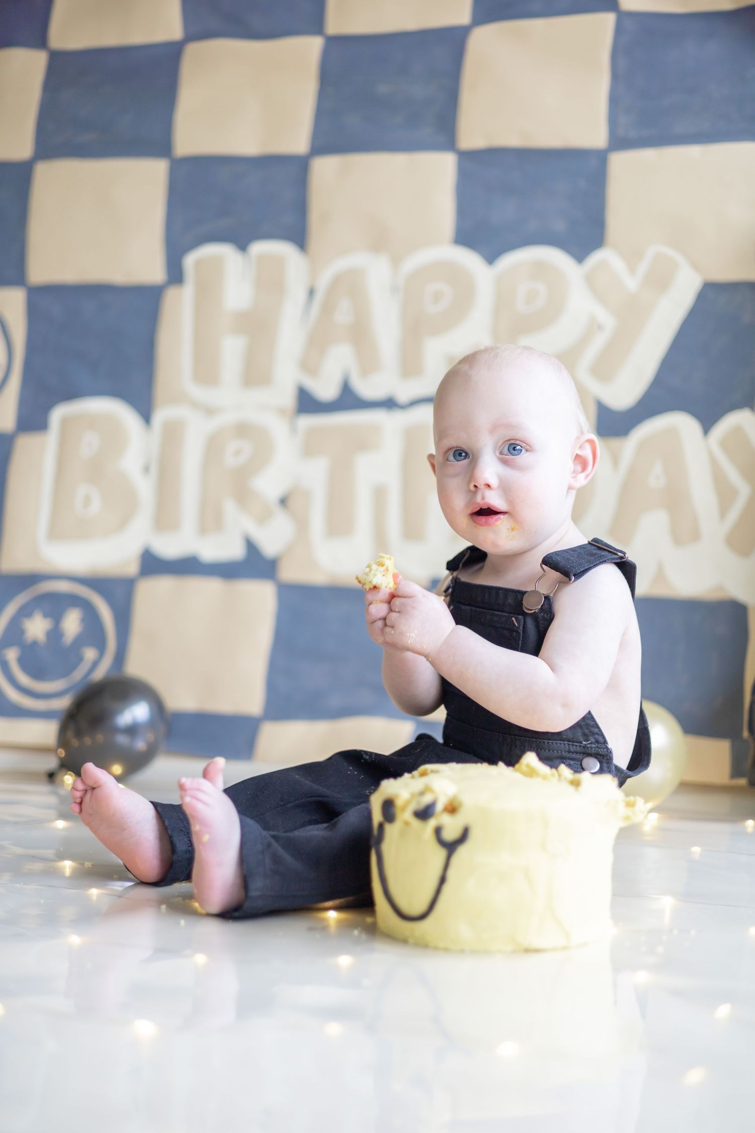 Four sequential images showing a baby in black clothing messy with cake celebrating their first birthday against a checkered wall.