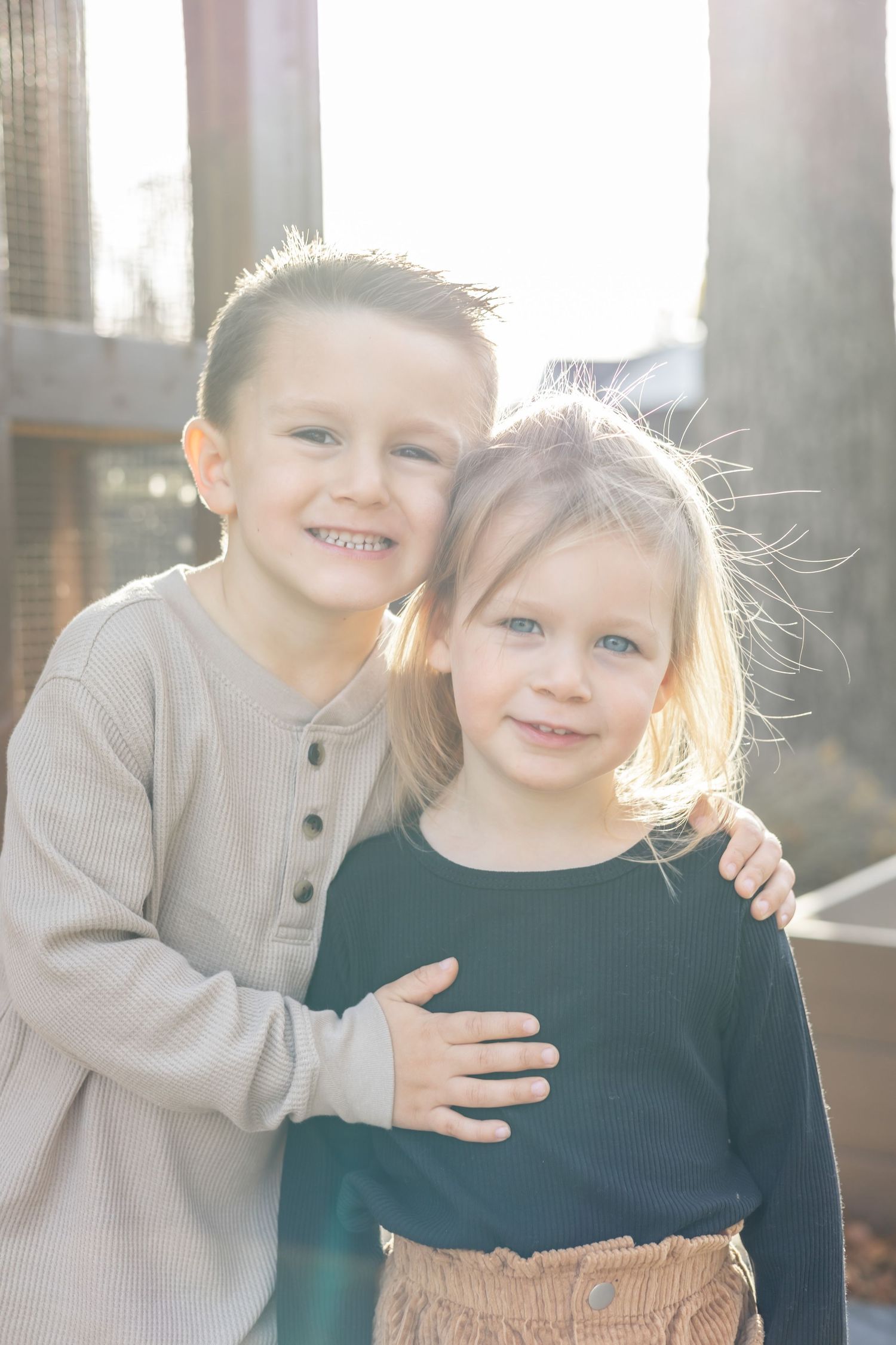 Two young children in casual attire share a sweet moment playing together outdoors in natural sunlight.