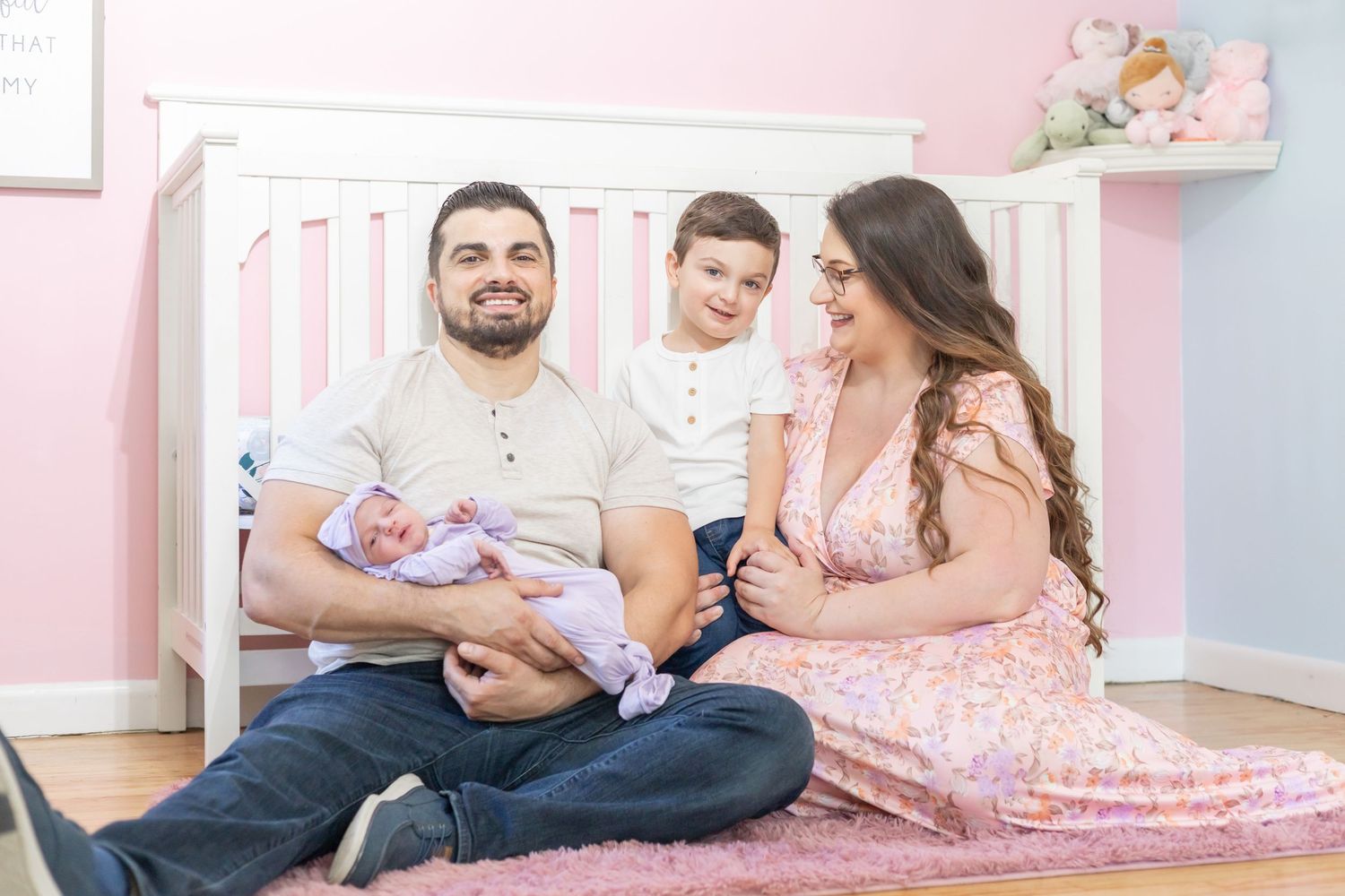 Parents sitting on floor of pink nursery with their two small children enjoying precious family time together.