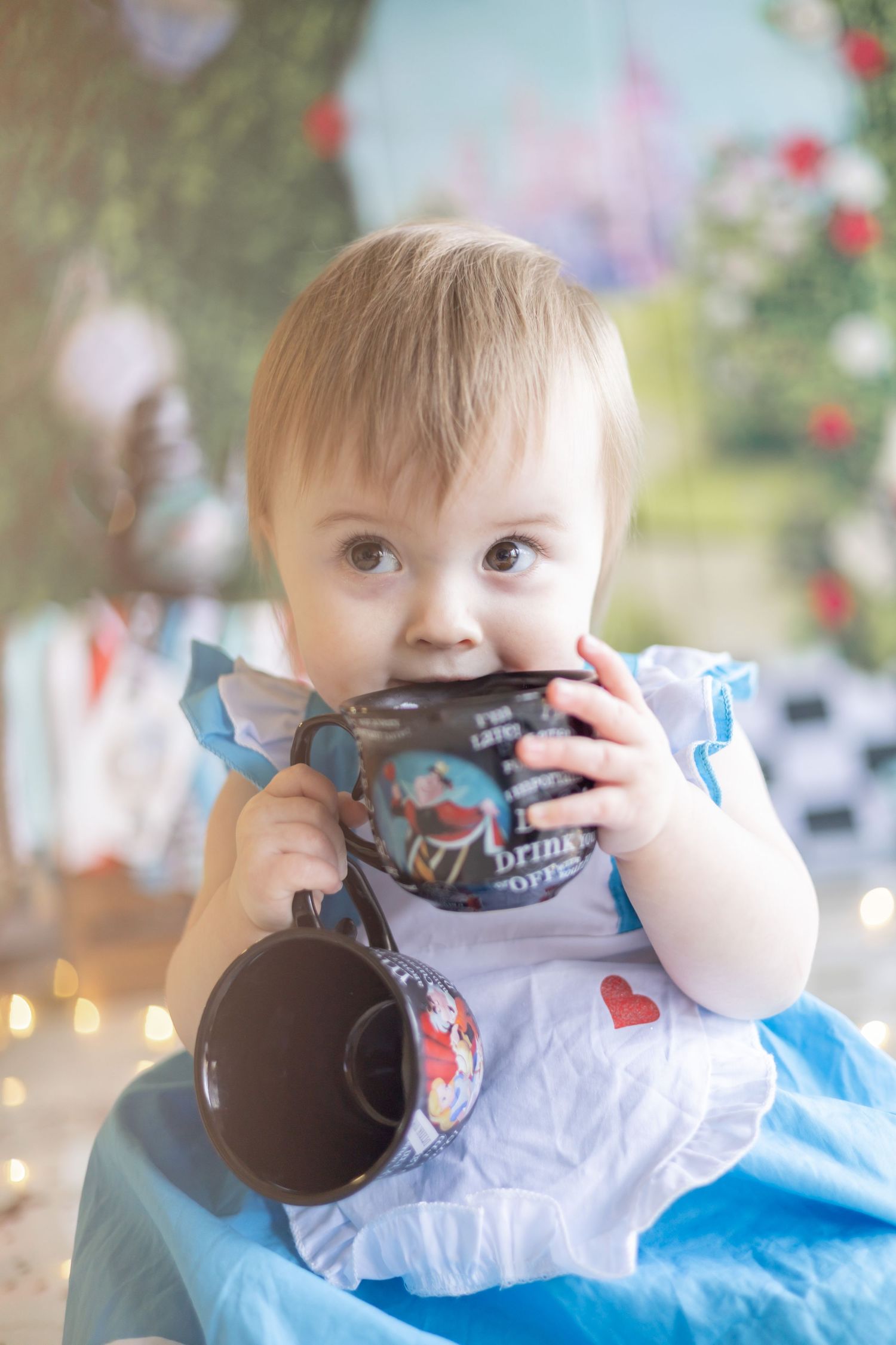 Baby in blue and white outfit sitting with black and white props against blurred floral background.