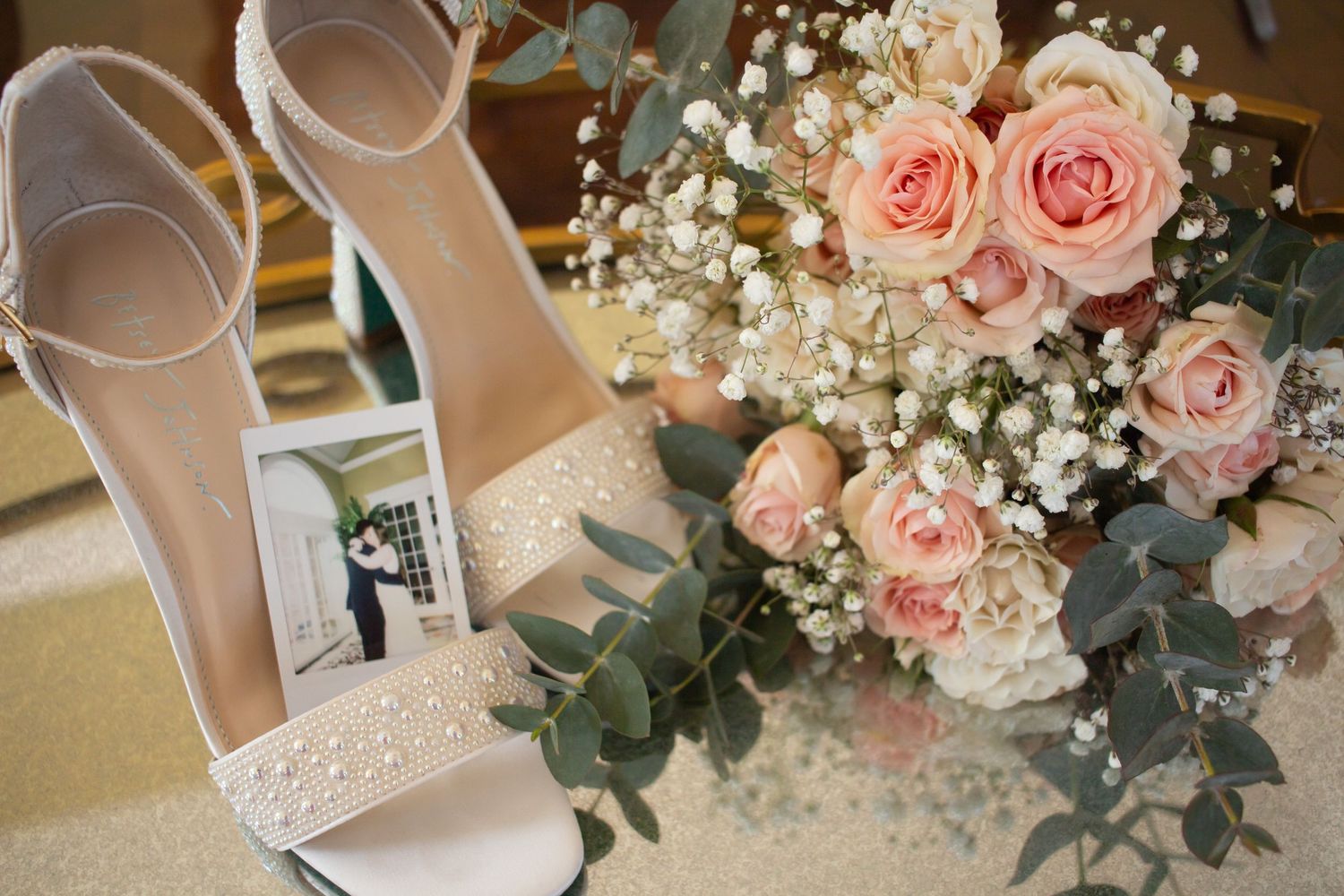 Elegant white lace wedding heels next to a soft pink rose and baby's breath bridal bouquet with eucalyptus.