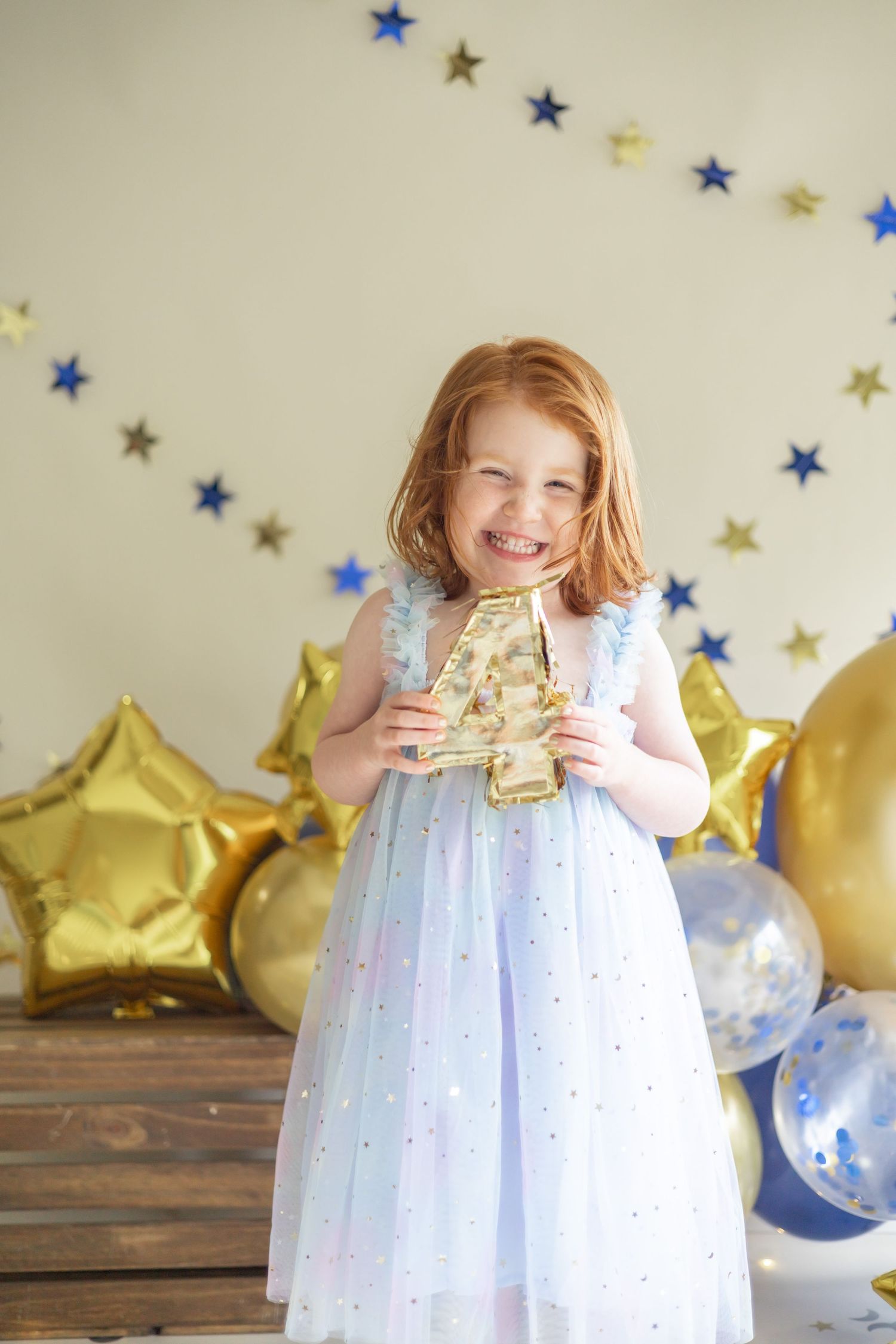 Festive party scene with sparkling gold stars, balloons and decorations against light background and wooden floor.