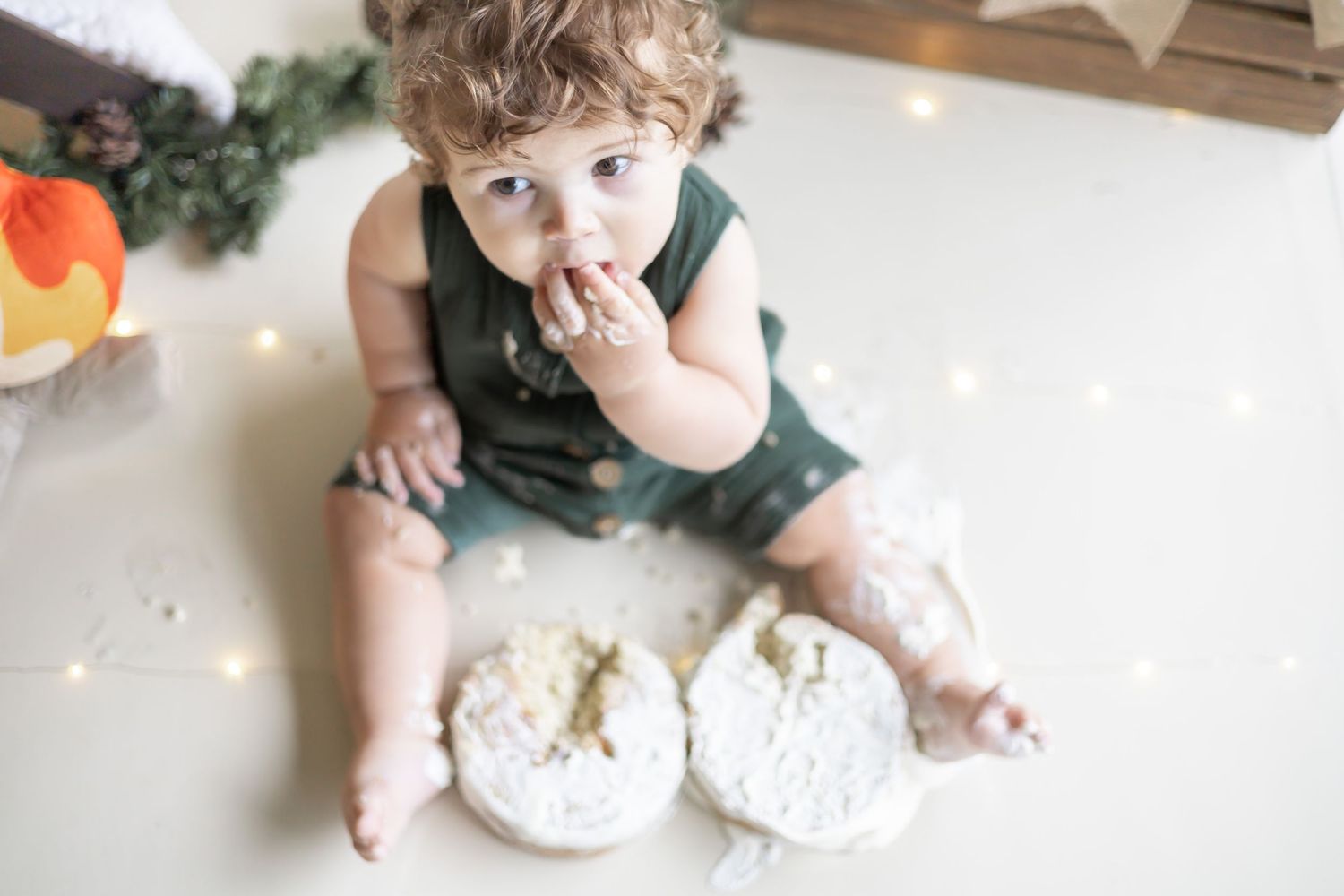 A baby in a green shirt sits and plays with messy food or dough spread across a white surface.