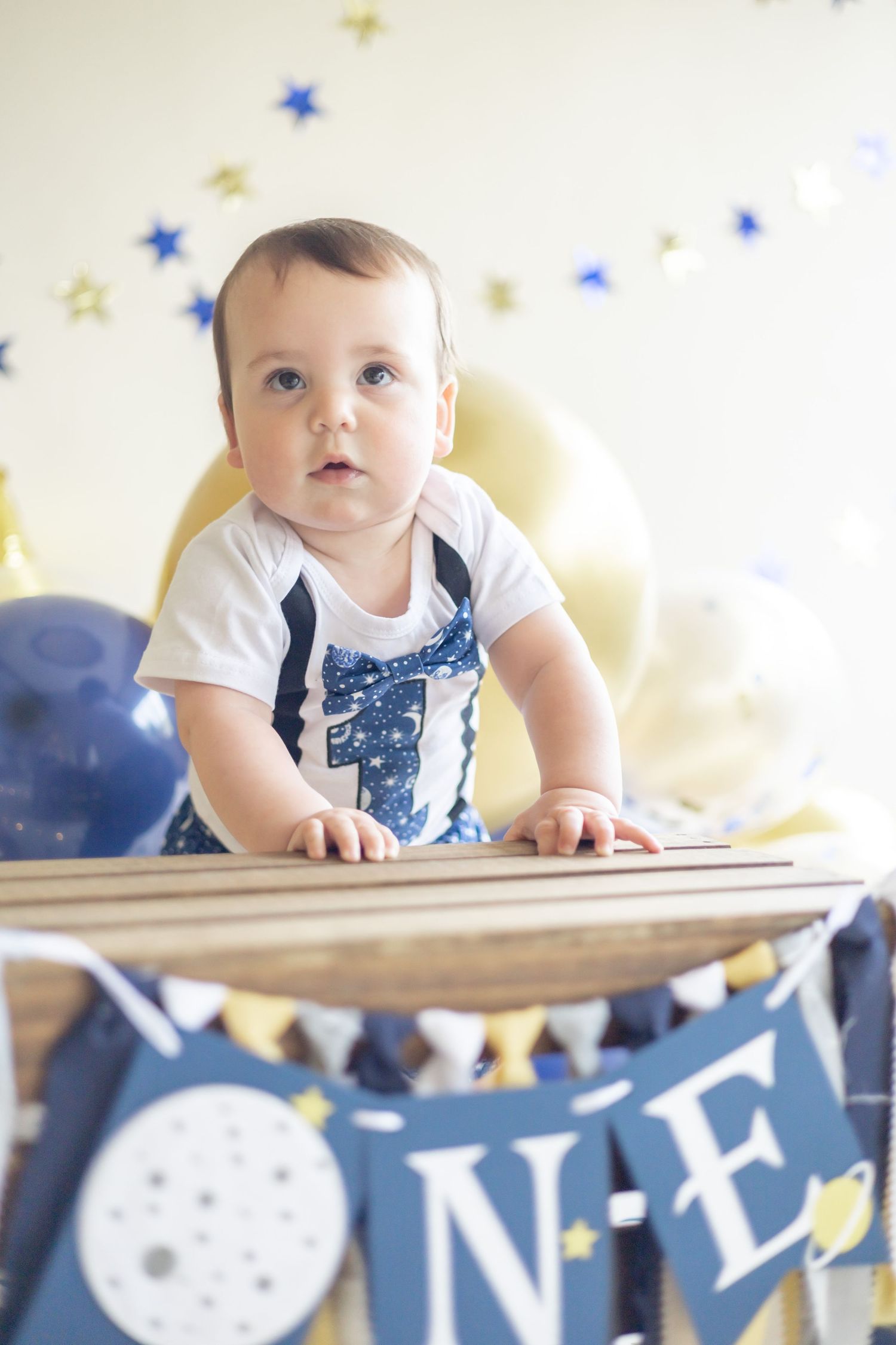 Baby in white and blue outfit crawls near decorative banner with blue stars and yellow embellishments.