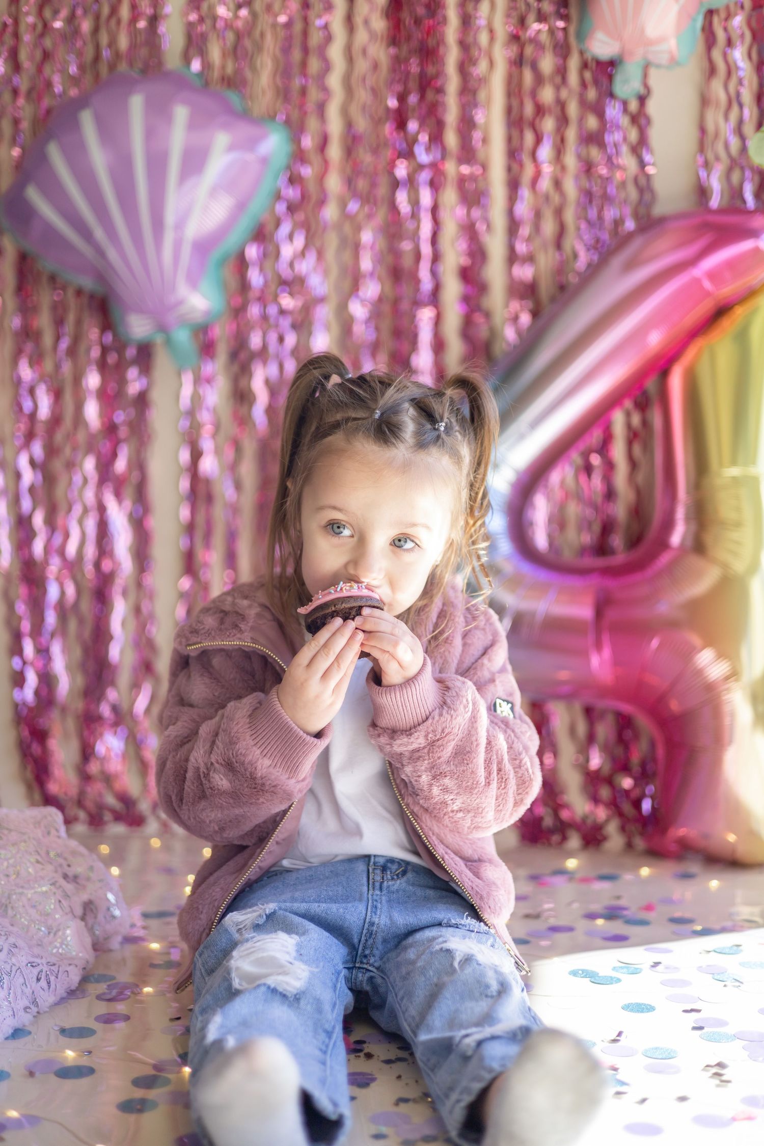 Festive celebration setup with seashell balloon, pink sequin backdrop, and cozy pink jacket.