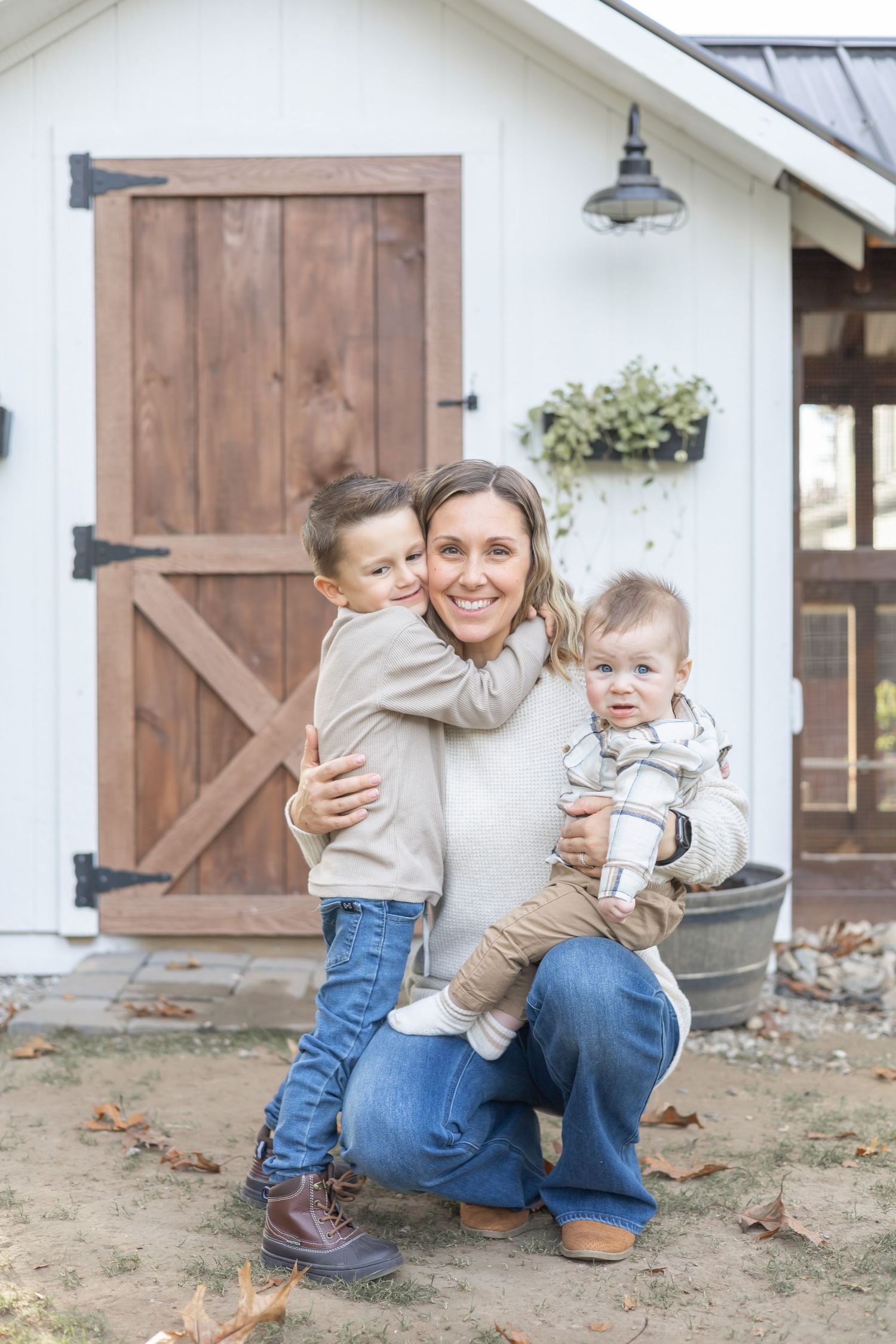 A warm family scene captured outside a farmhouse with wooden barn door and rustic lighting fixture.