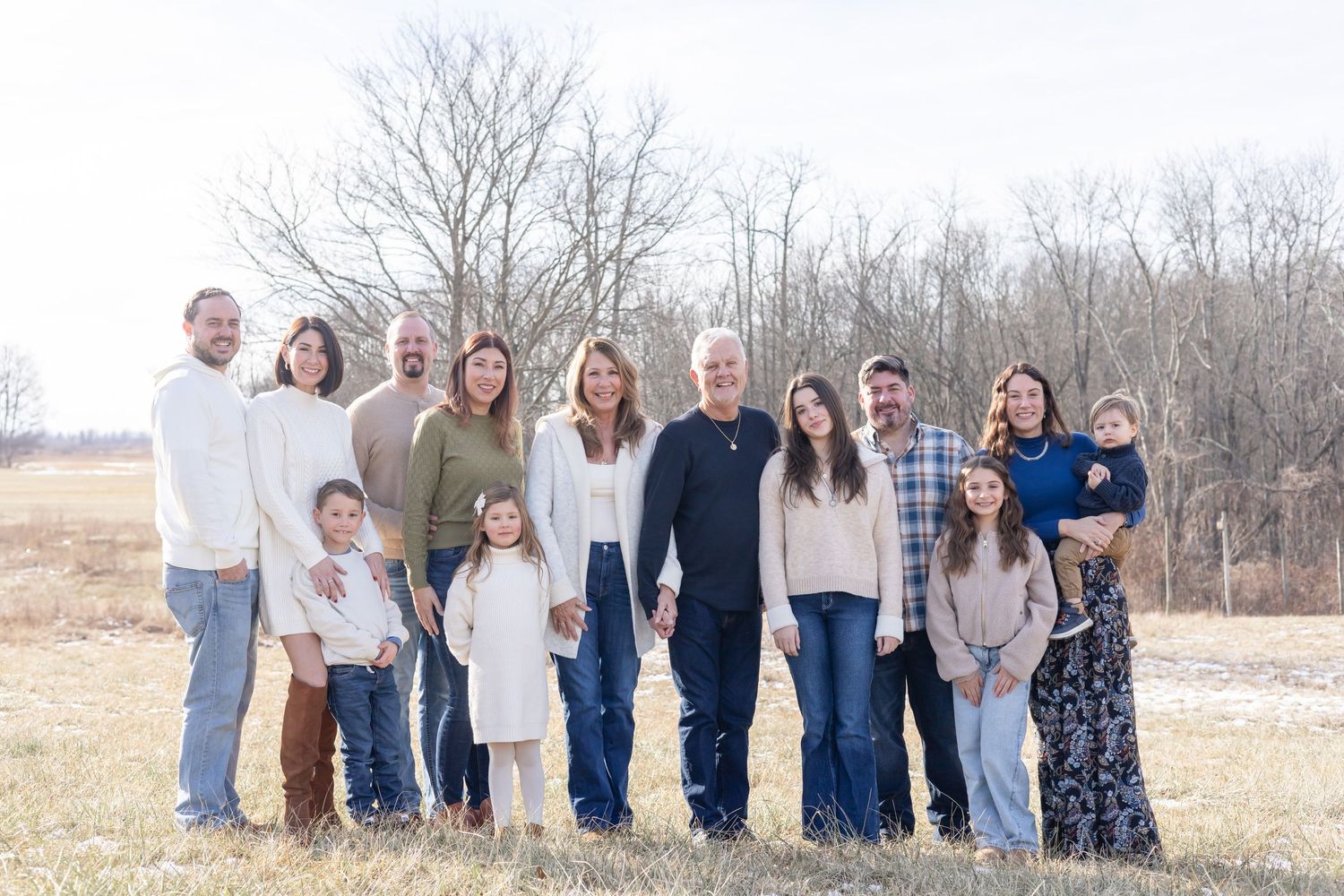 A group of people wearing coordinated casual outfits stands together in a field on an overcast winter day.
