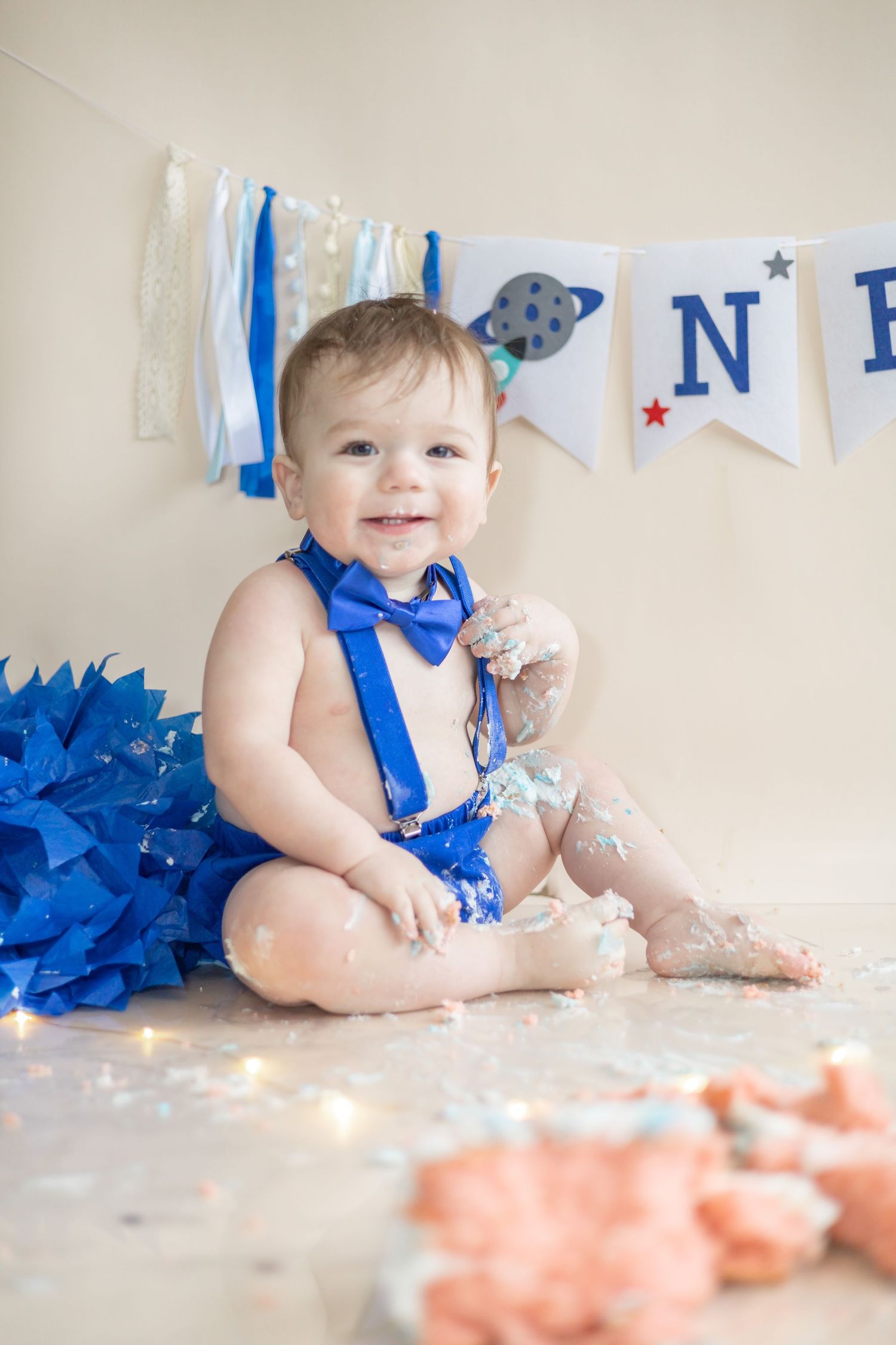 A young child in blue attire sits on floor with party decorations and lights during a festive celebration.