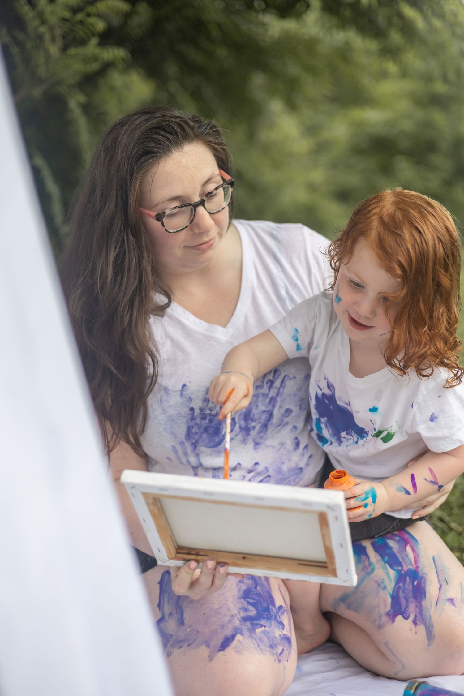 Two people paint together outdoors getting messy with blue paint while creating art on a small canvas.