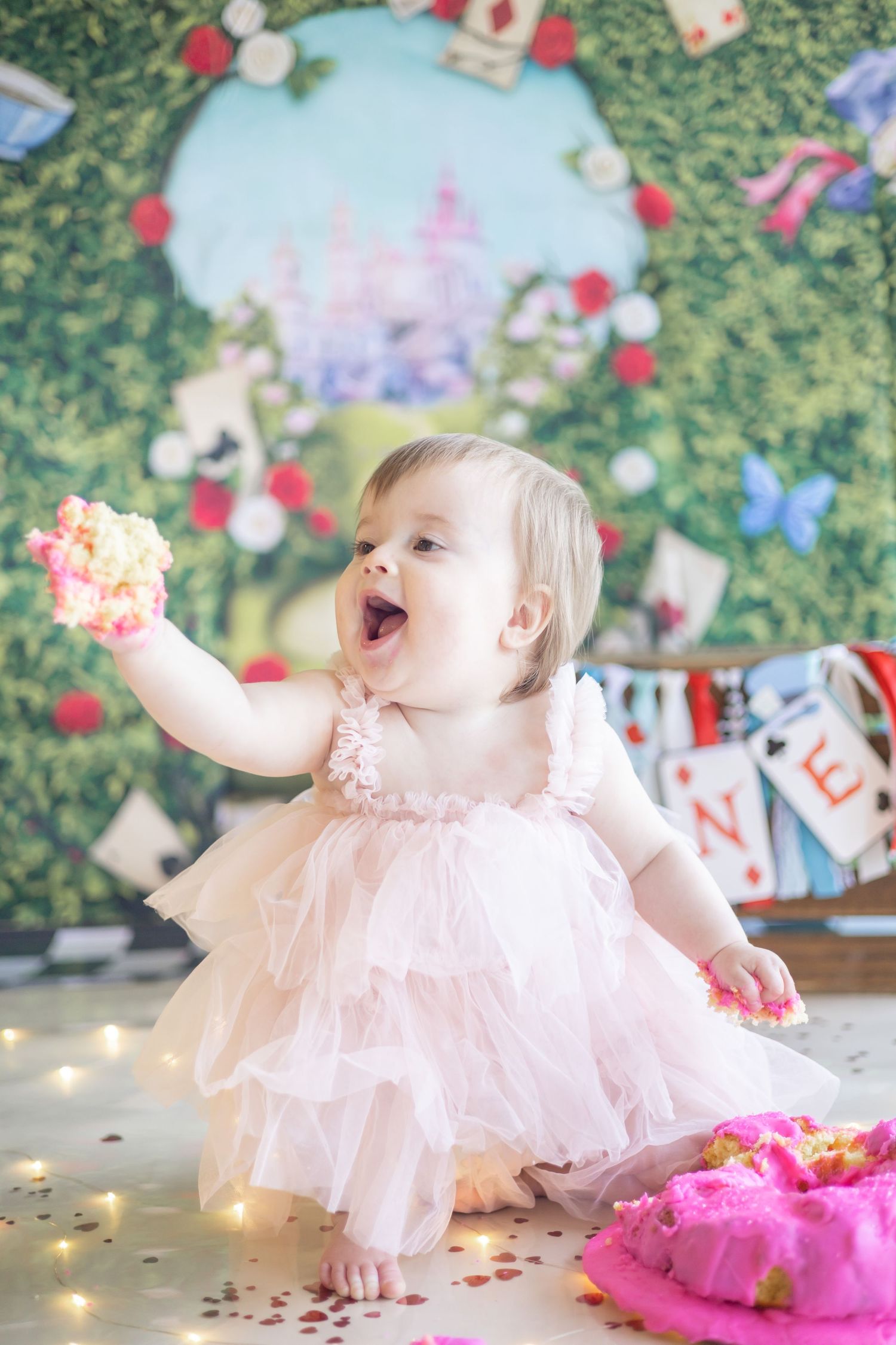 A baby in a pink tulle dress plays with cake and confetti during a cake smash photo session.