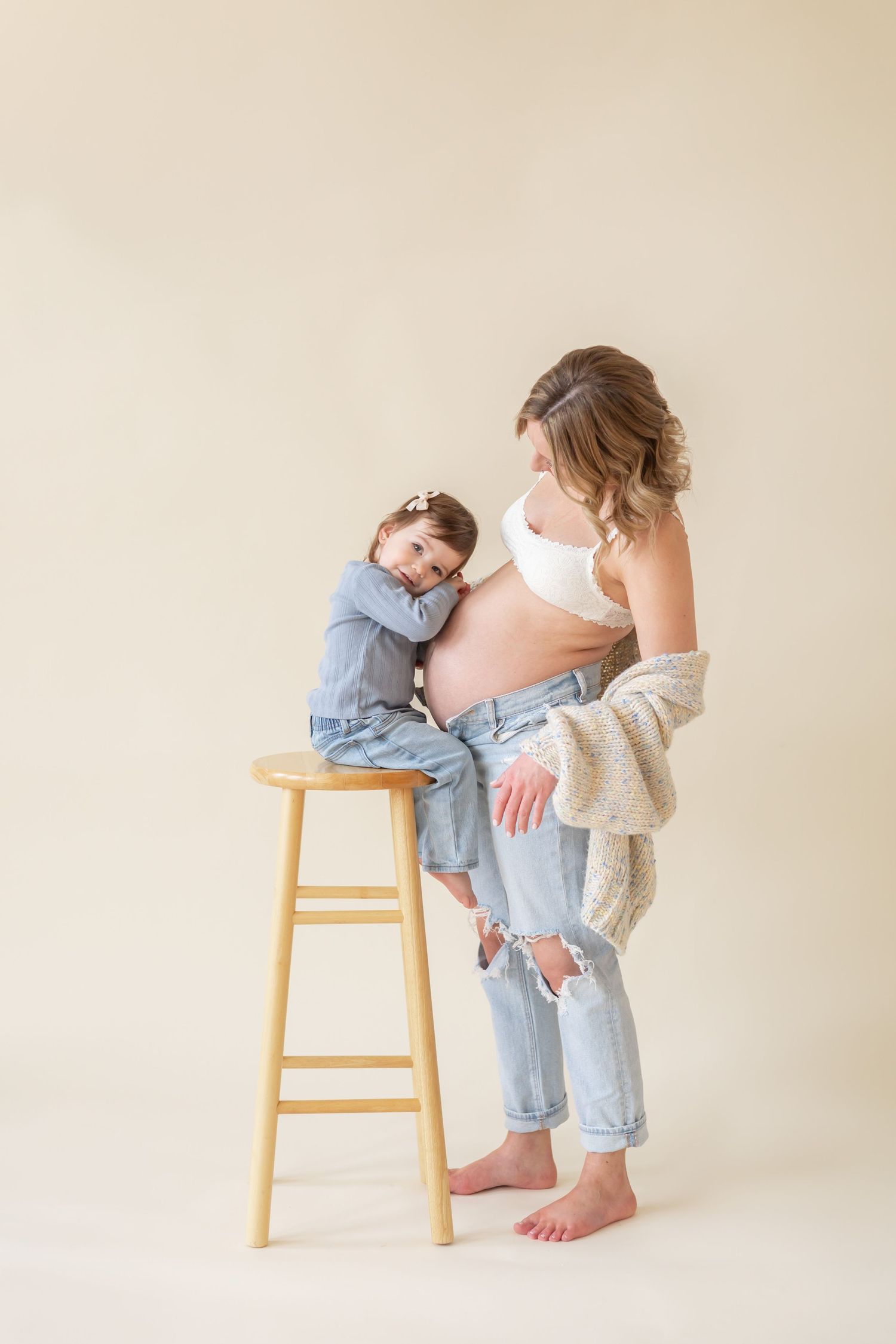 A sweet and intimate pregnancy photo shoot sequence showing a tender moment between mother and small child by a wooden stool.
