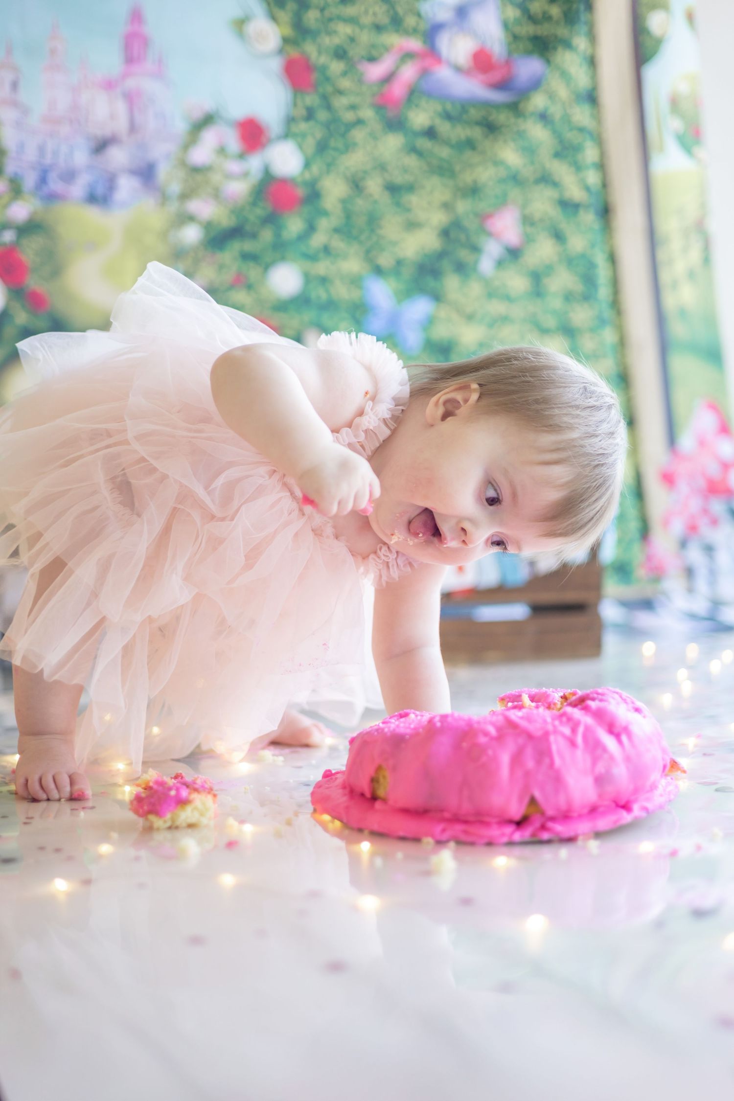 Baby in pink tutu plays with bright pink cake during first birthday cake smash photo session.