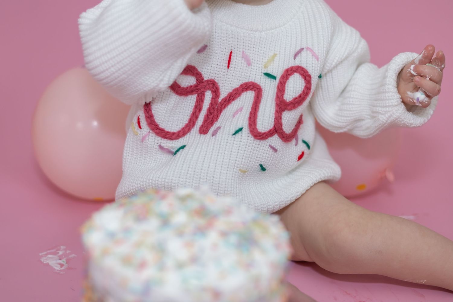 Small hands play with colorful pastel cream and pink textured elements against a soft pink background.