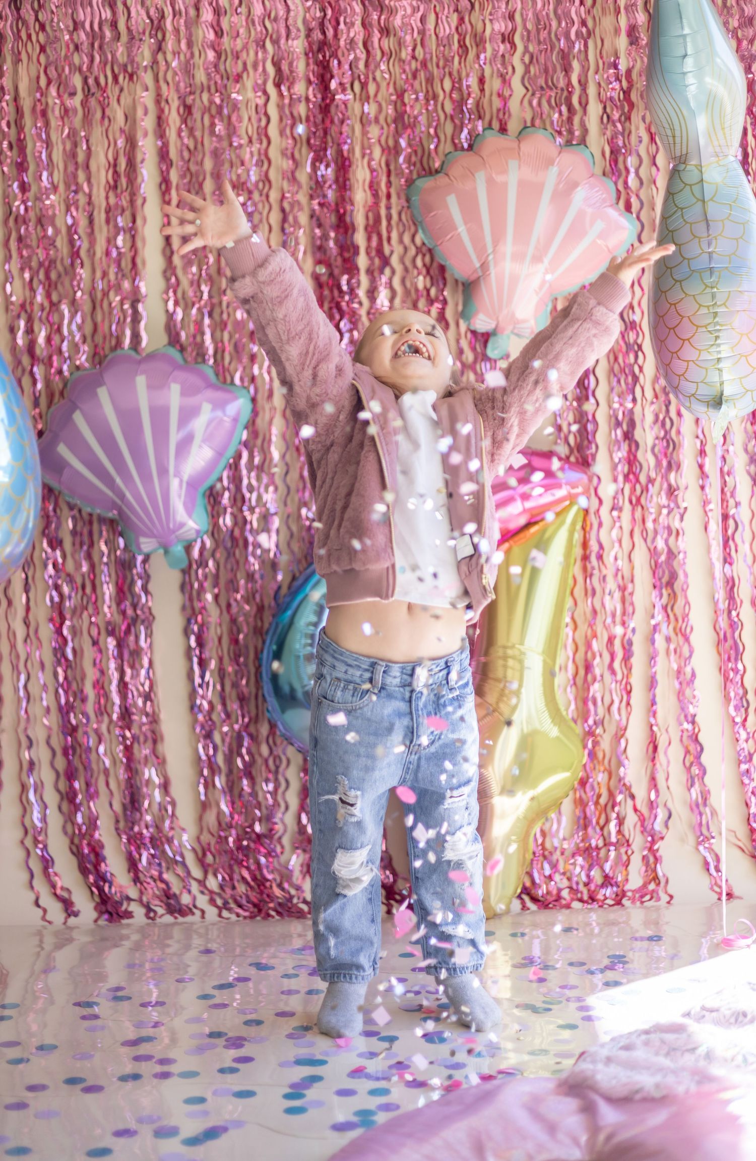 Joyful celebration scene with pink streamers, shell-shaped balloons, and confetti against a sparkly backdrop.