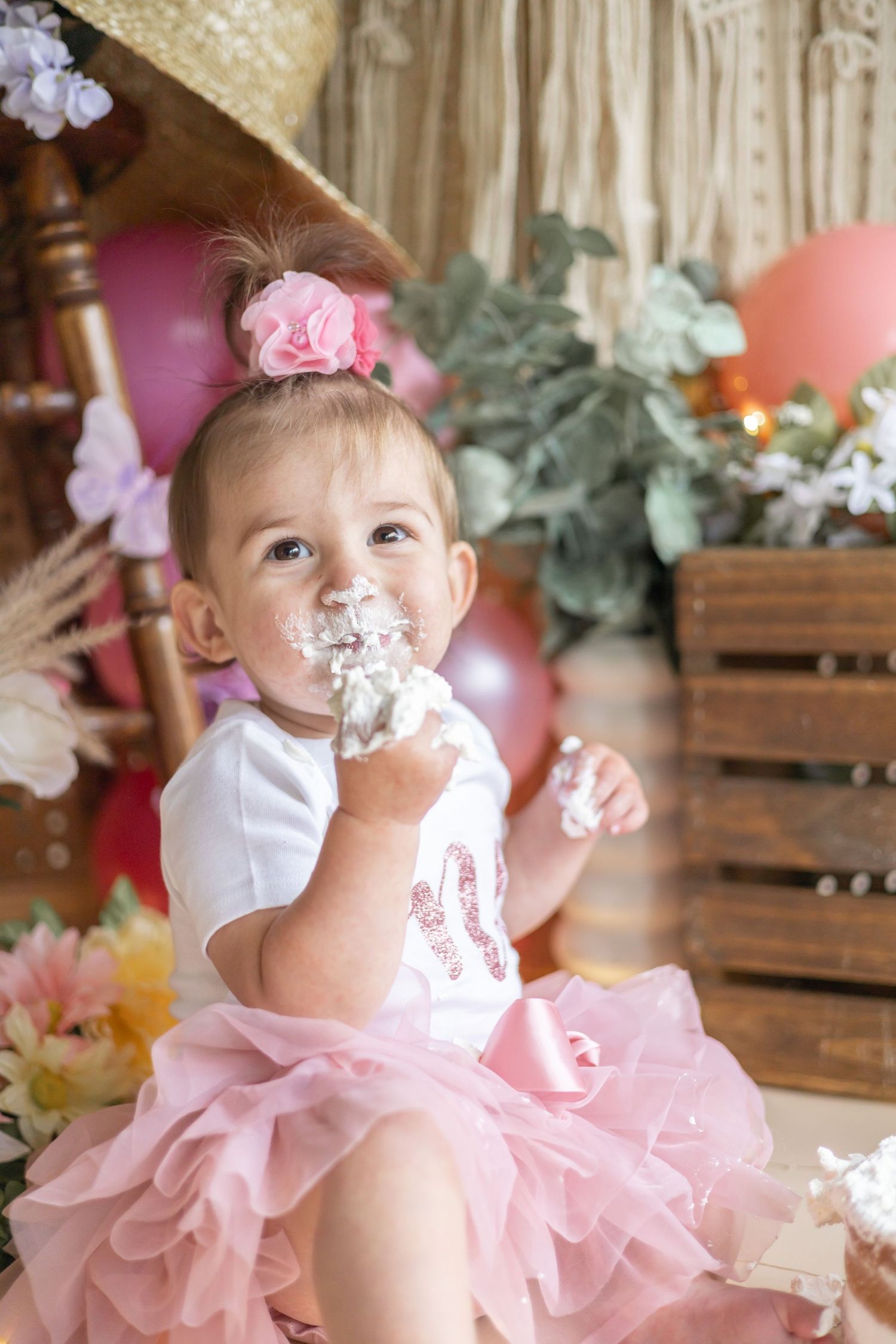 Toddler in pink tutu dress and white top enjoys cake with frosting on their face during a celebration.