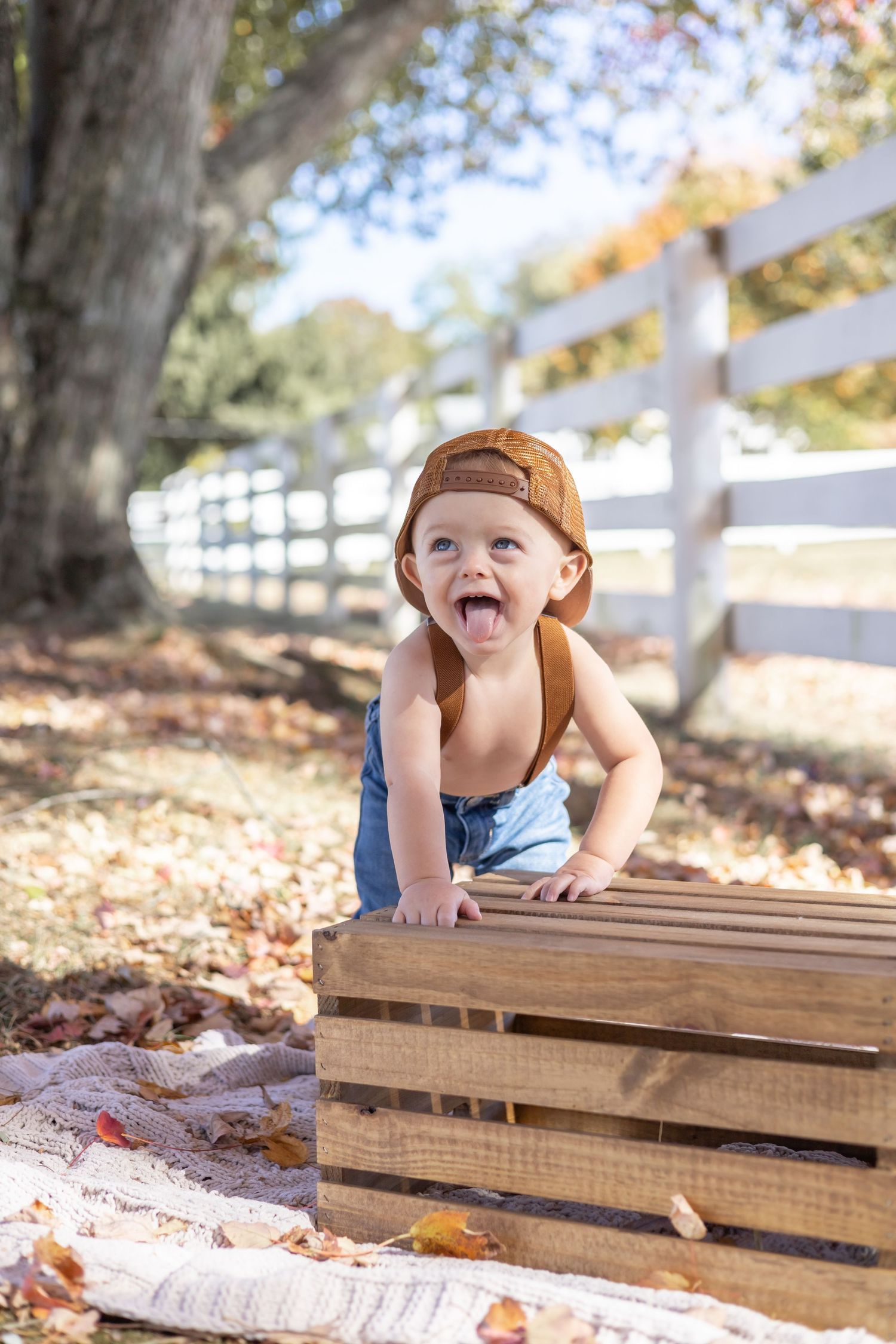 A playful child lies on a wooden bench surrounded by autumn leaves on a sunny day.