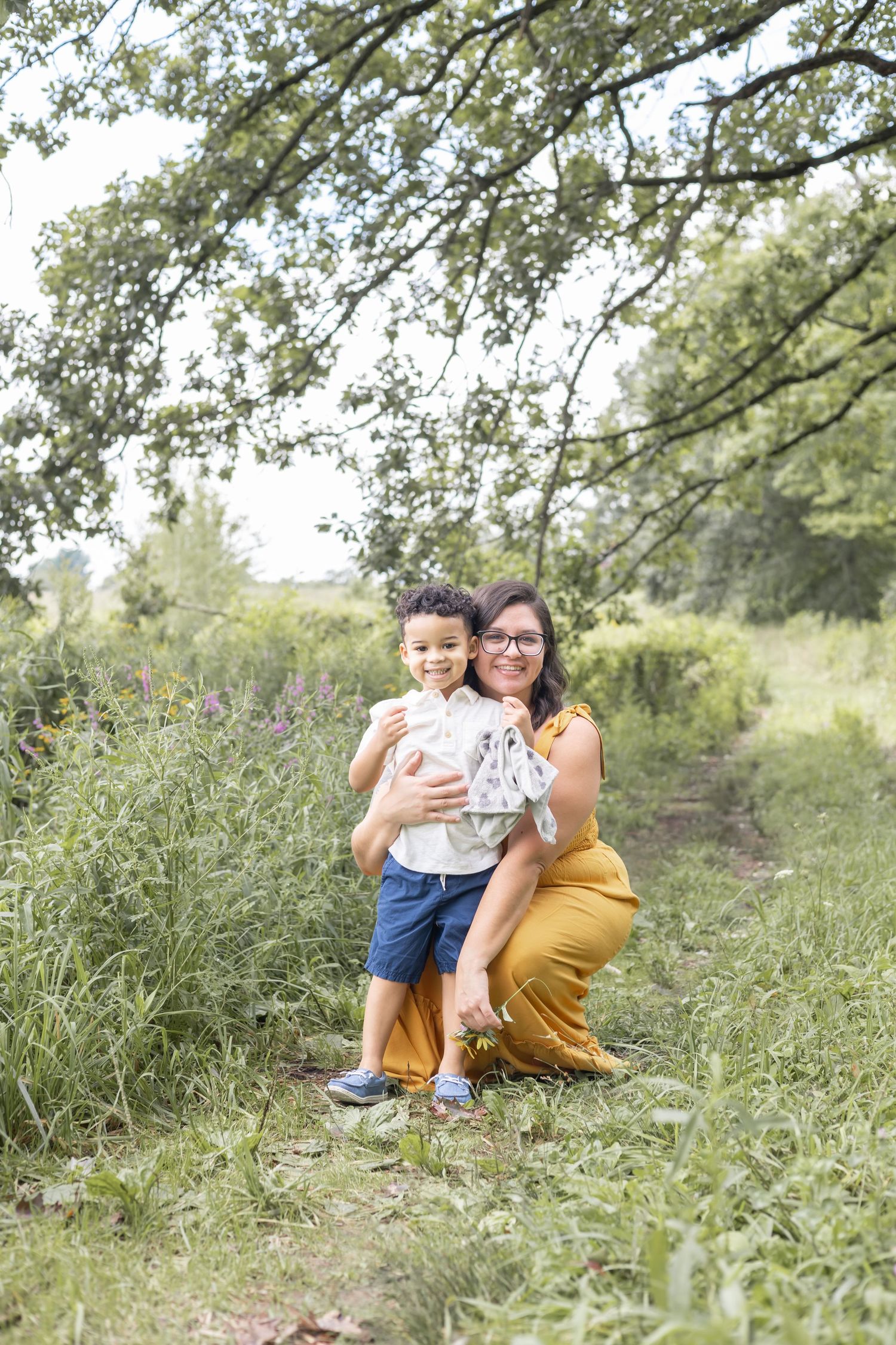 A peaceful outdoor family portrait in a natural setting with tall grass and trees.