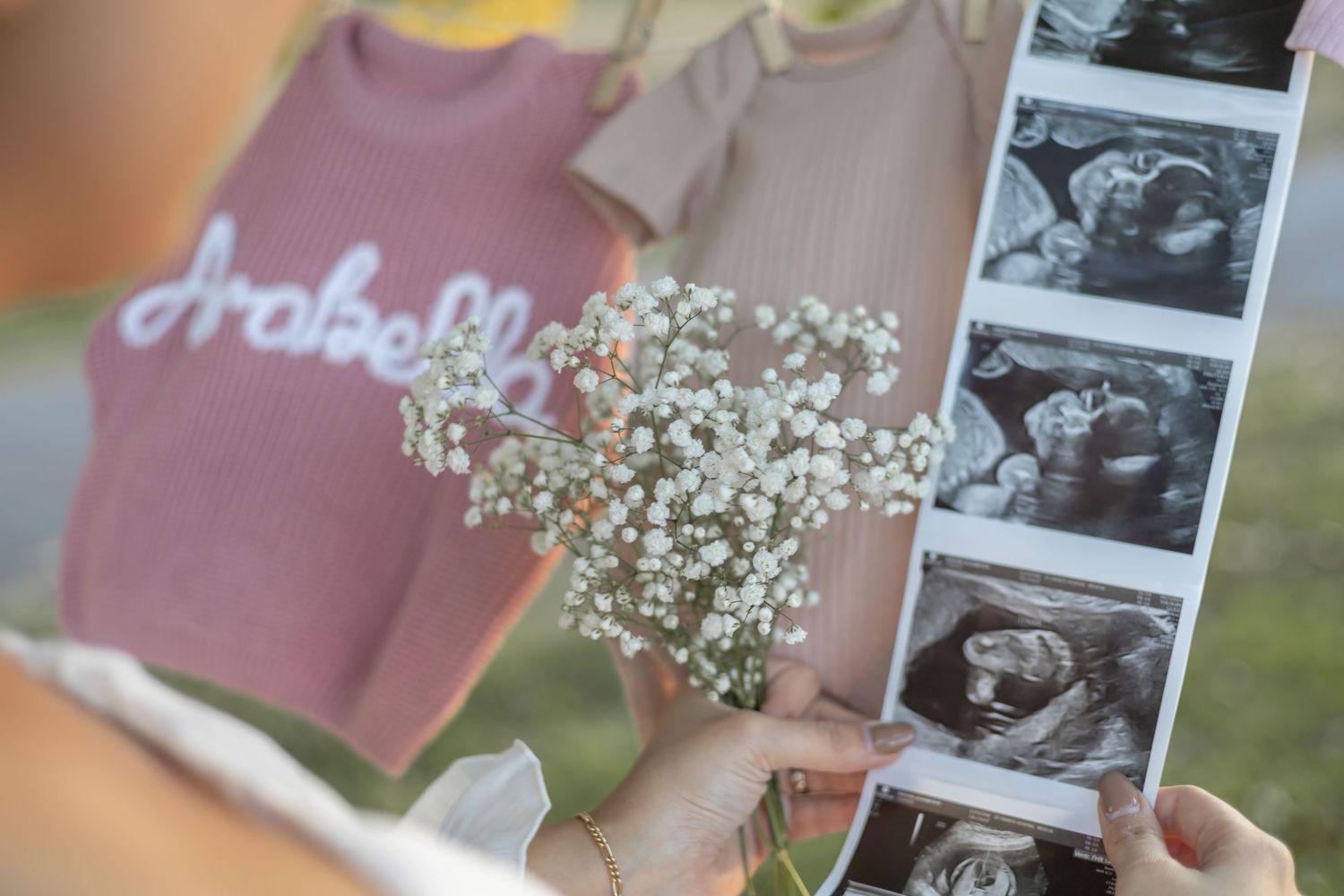Baby announcement photos with ultrasound pictures and delicate white flowers against a soft pink backdrop.