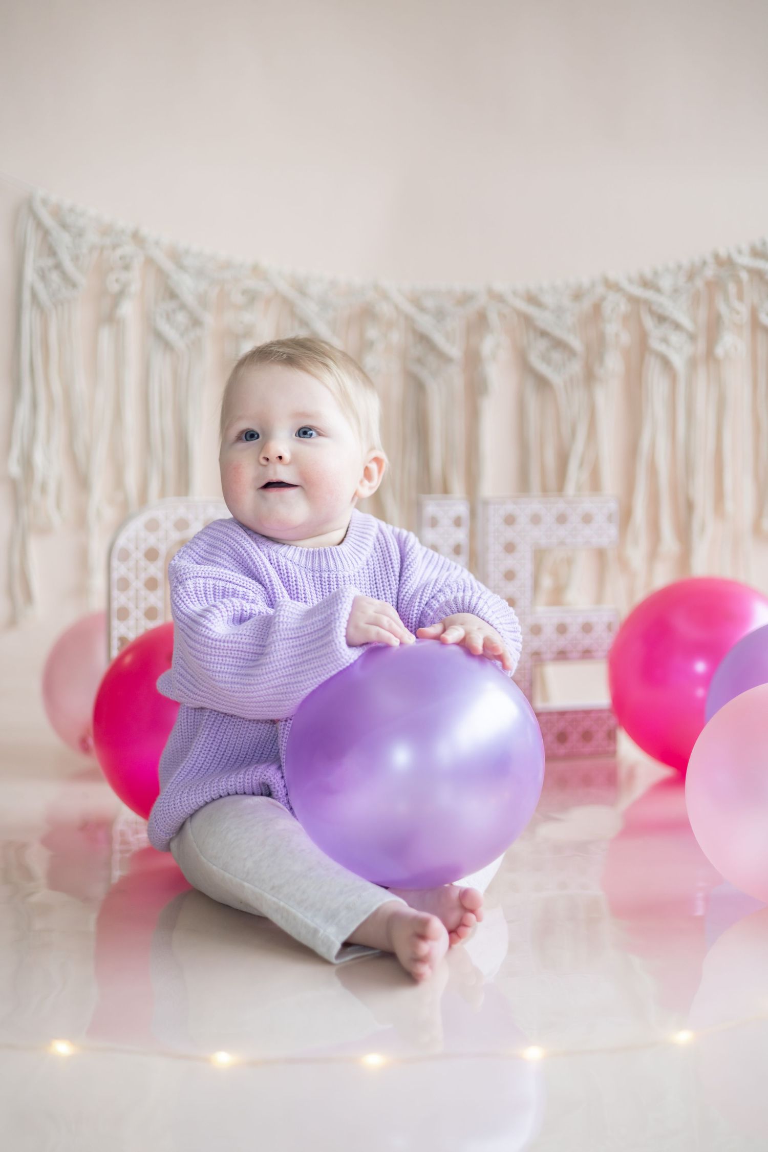 A series of four connected images showing a baby in purple clothing playing with pink and purple balloons on a white floor.