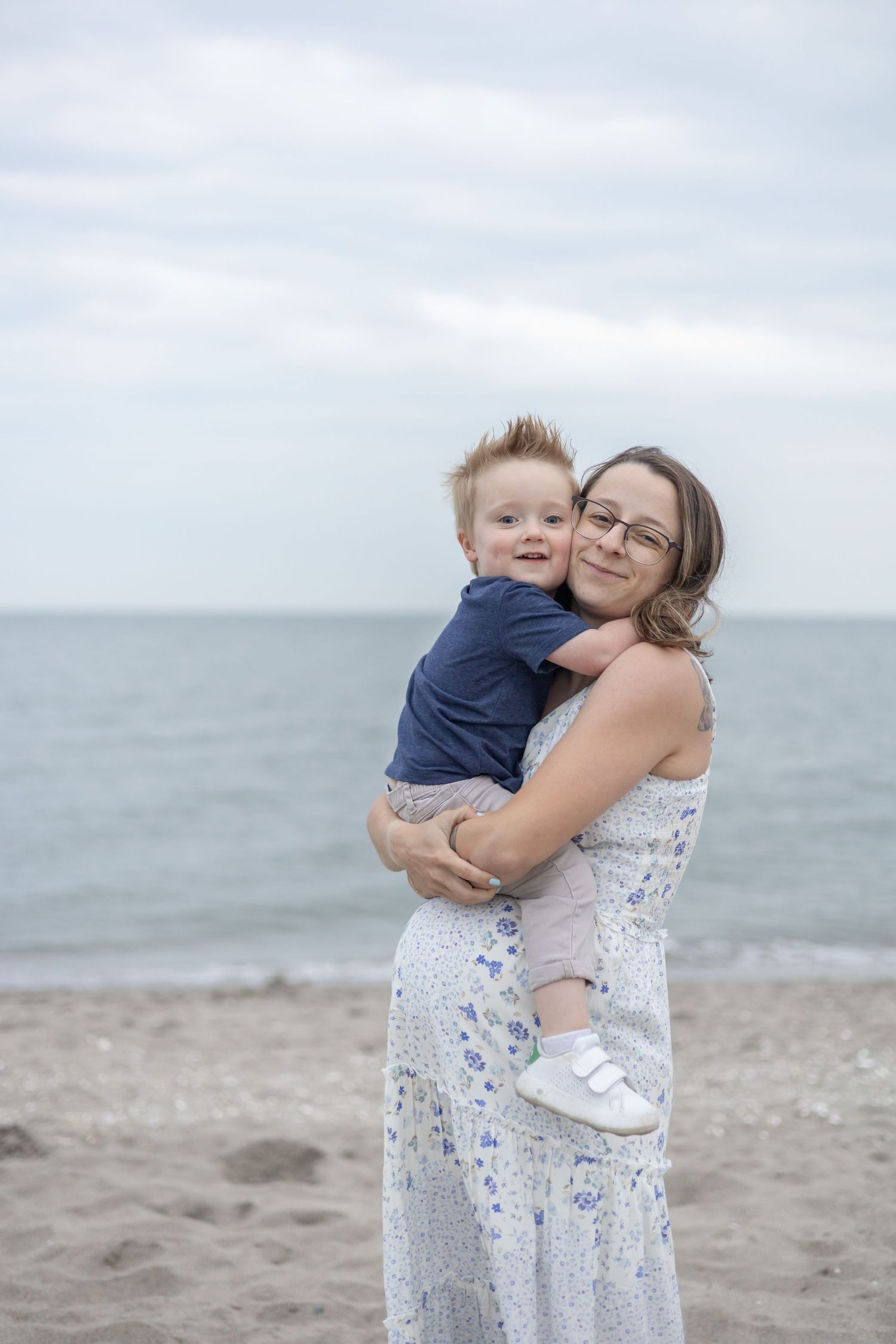 A tender moment shared between two people embracing on a peaceful, cloudy beach with ocean waves in the background.