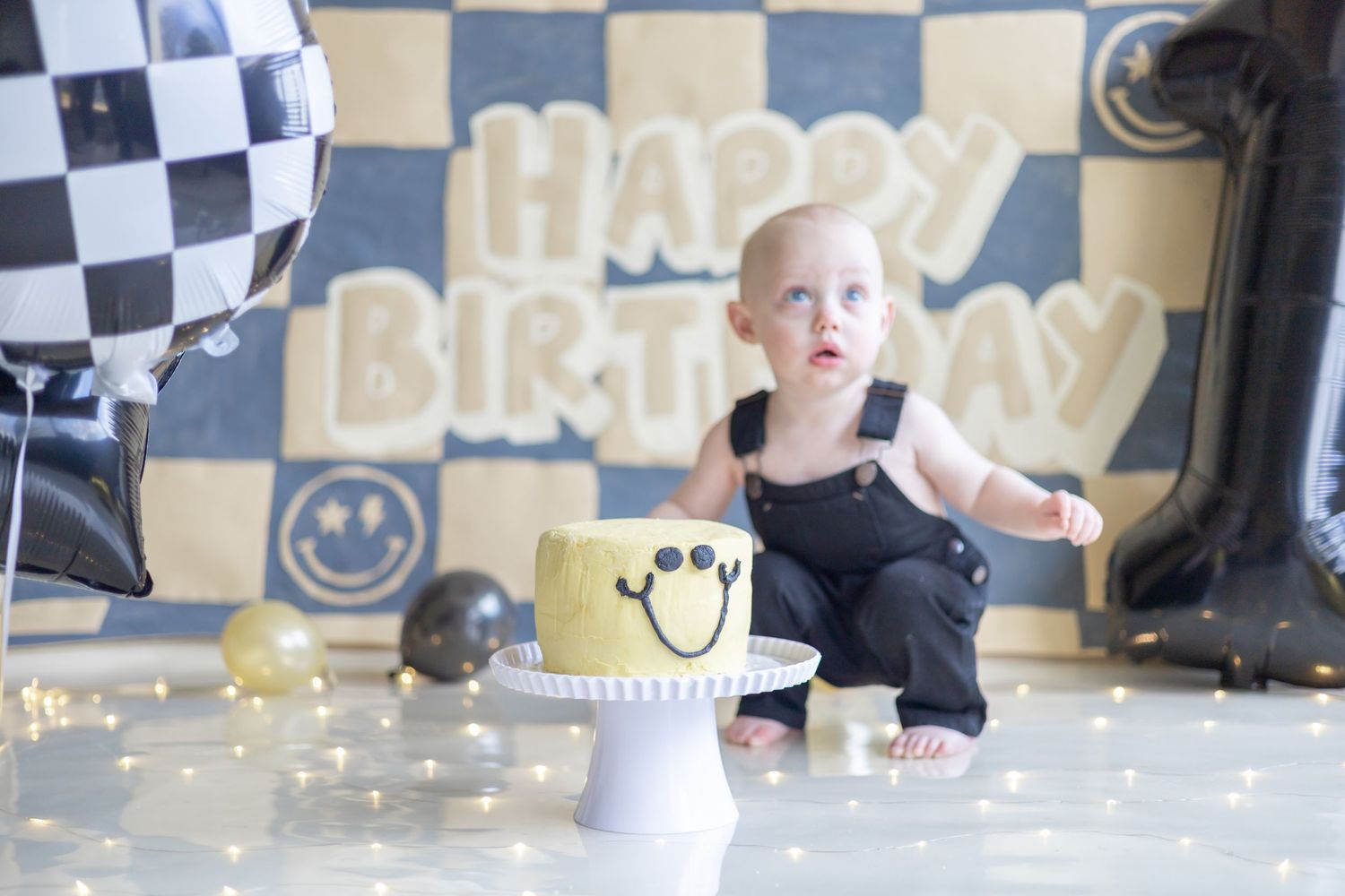 A festive cake smash birthday photo session with black and white checkered decor and a white smash cake.