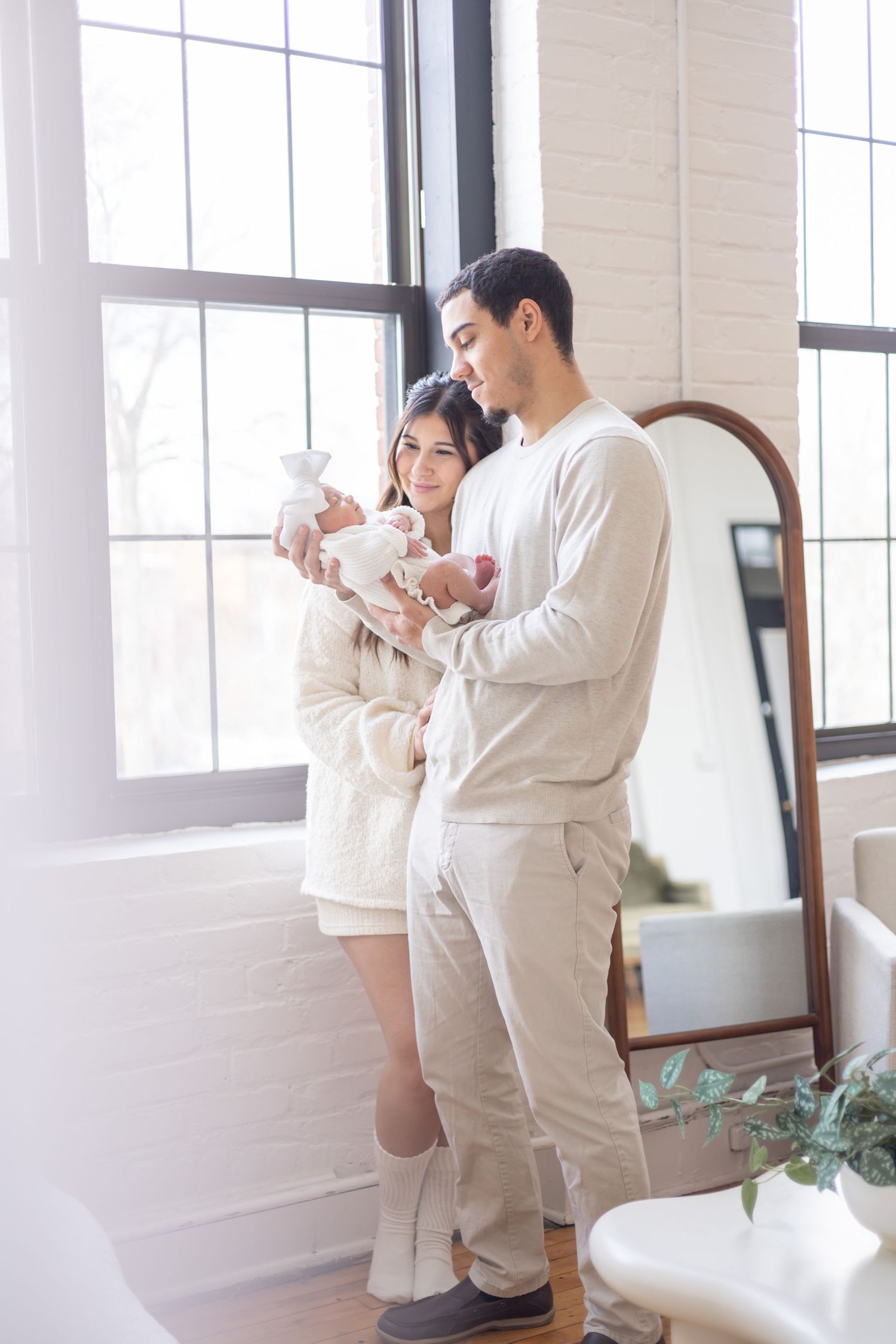 Two people in white matching outfits stand and interact in a bright room with large windows.