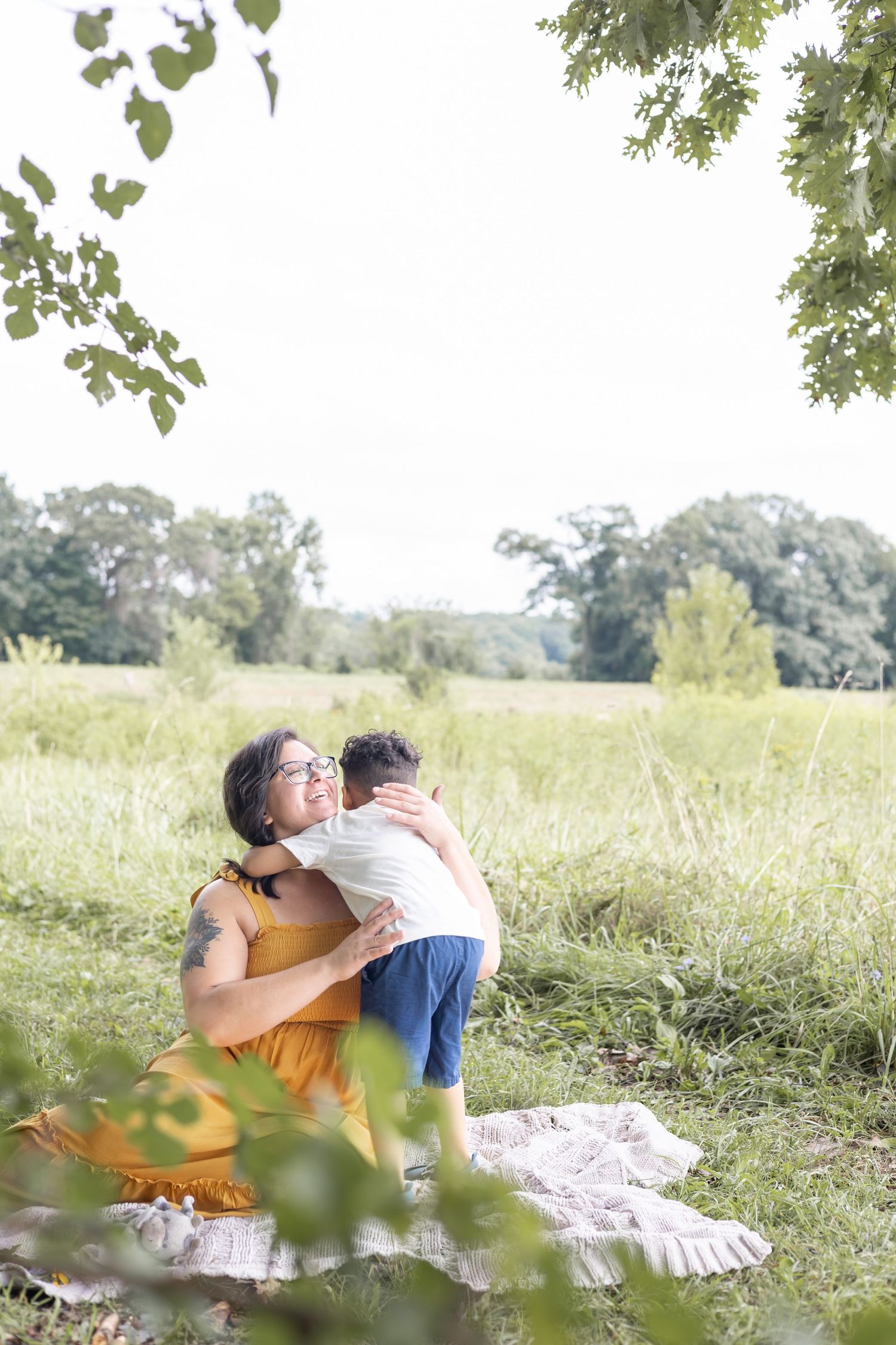 A tender moment shared on a picnic blanket in a sunlit meadow surrounded by trees.