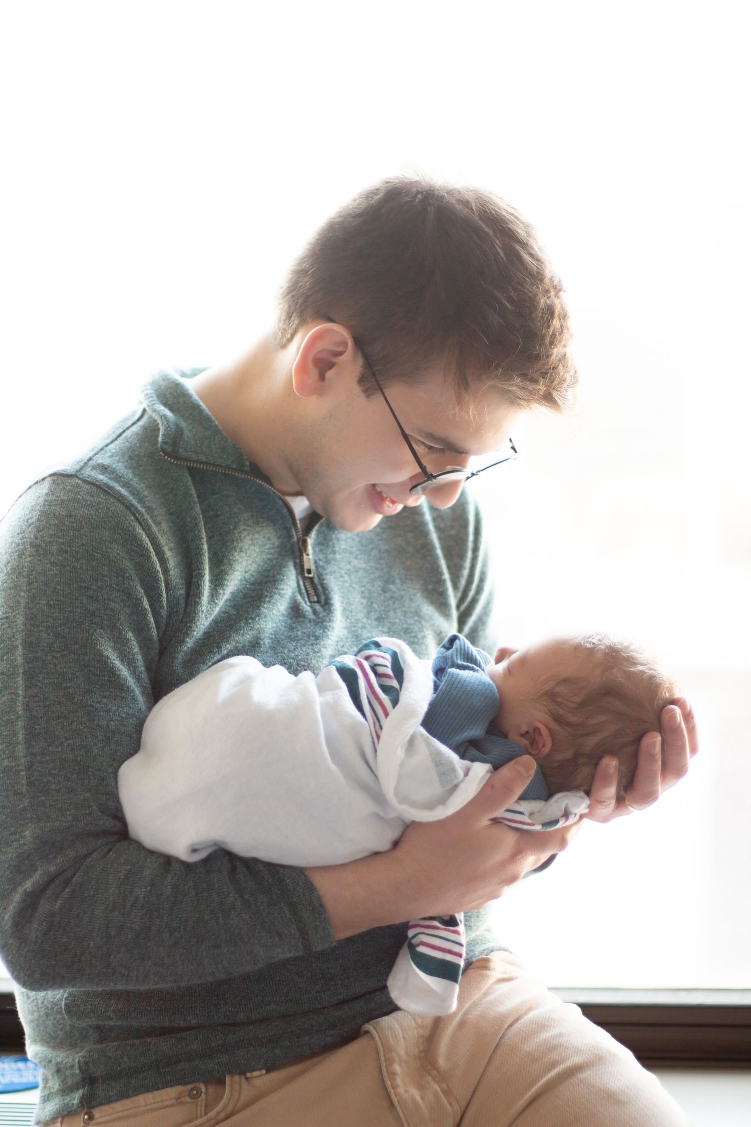 A person in a green sweater tenderly holding and gazing at a newborn baby wrapped in white blankets.
