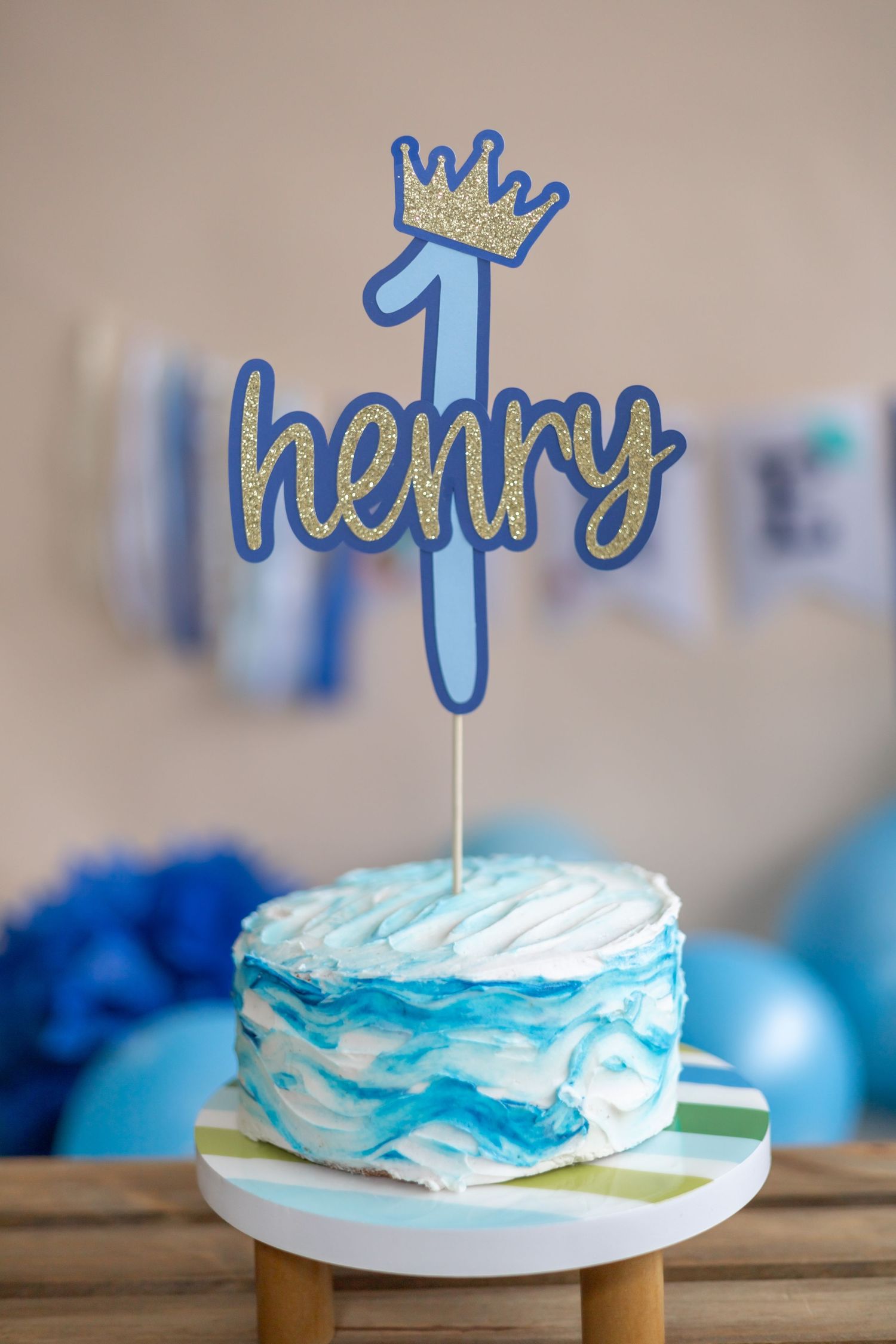 A blue and white frosted cake with a crown-shaped topper shown from different angles on a wooden surface.