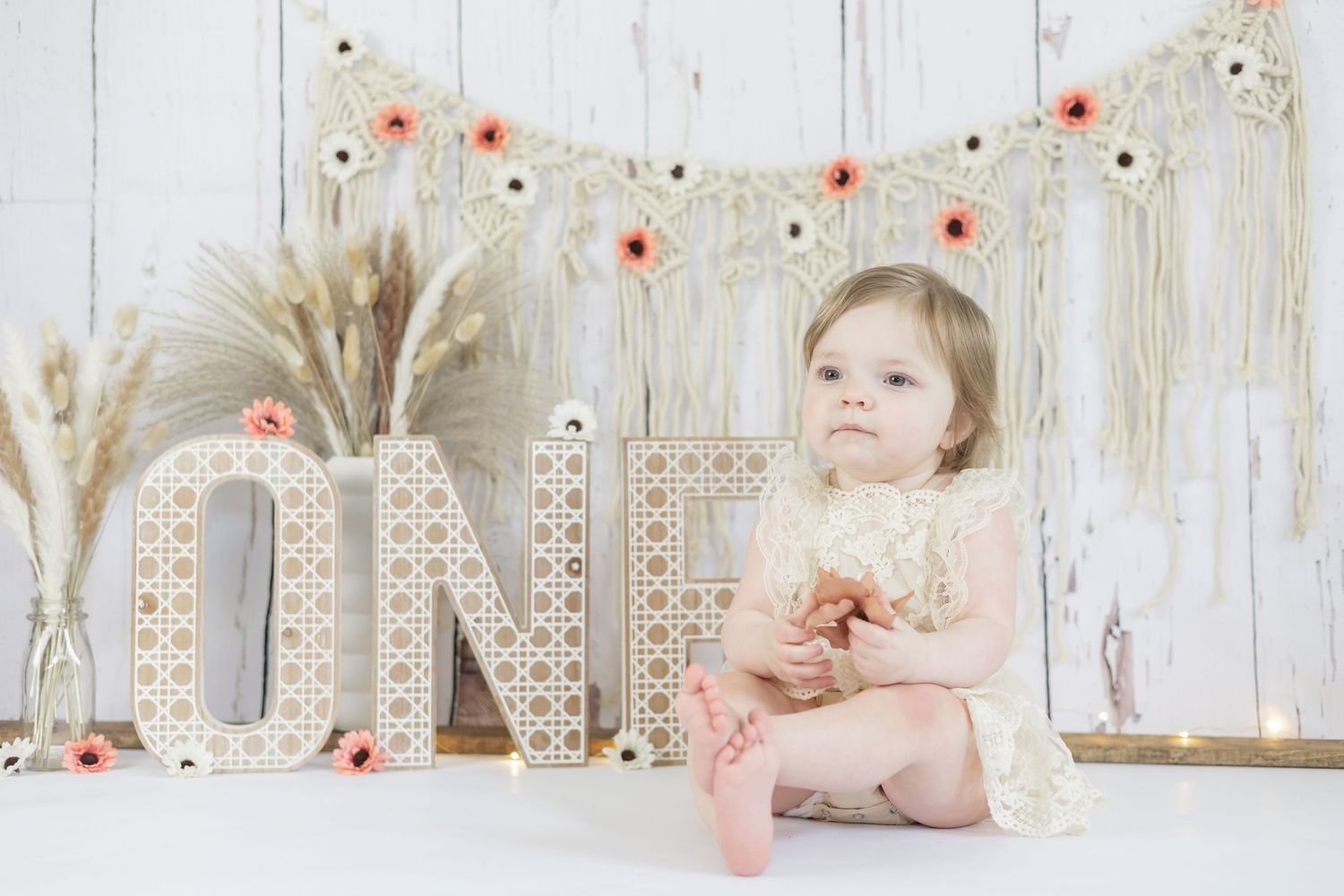 First birthday photo setup with rustic white decorative letters and red floral garland against whitewashed backdrop.