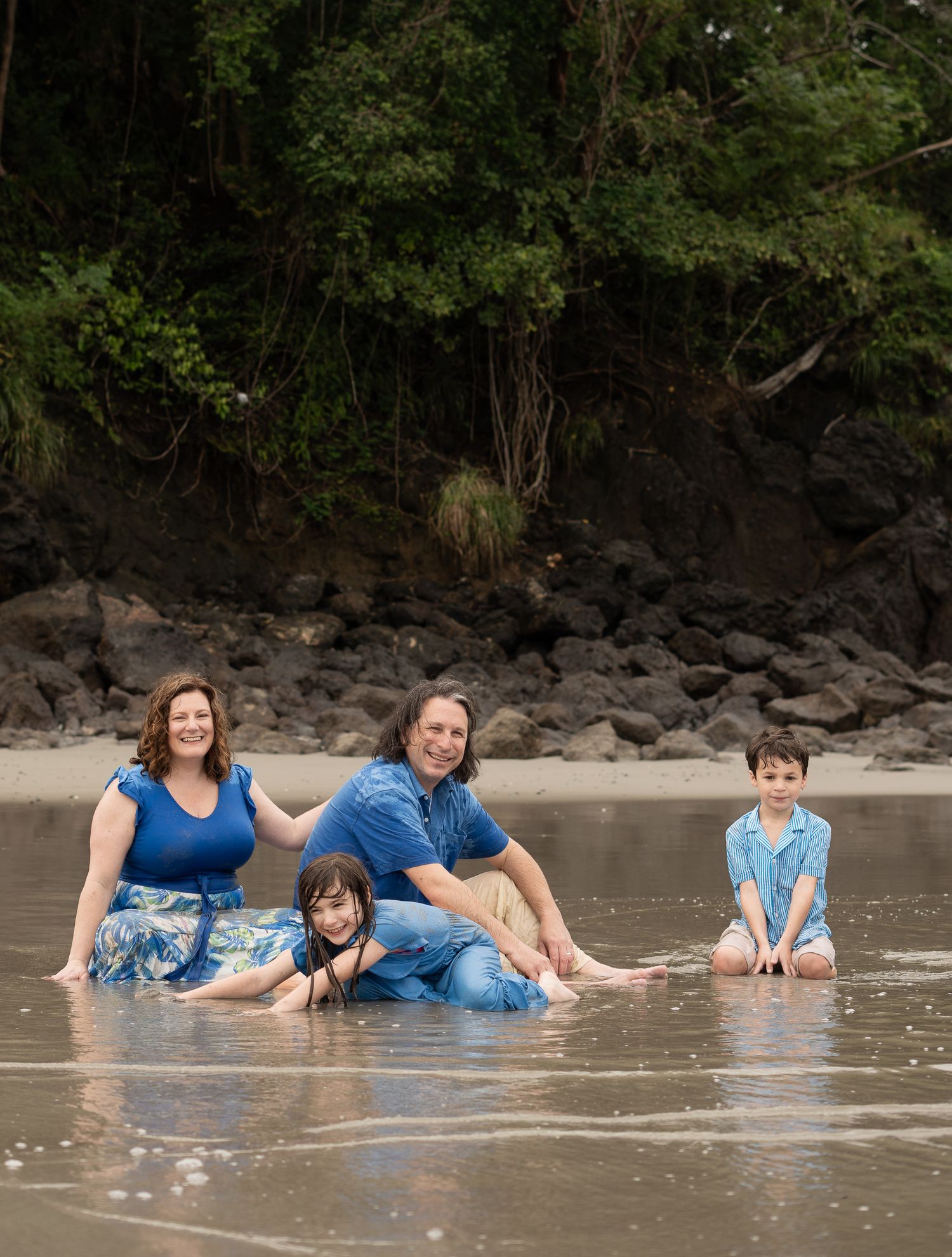 Group enjoying a playful moment lying in shallow beach water wearing blue outfits. Manuel Antonio, Costa Rica.