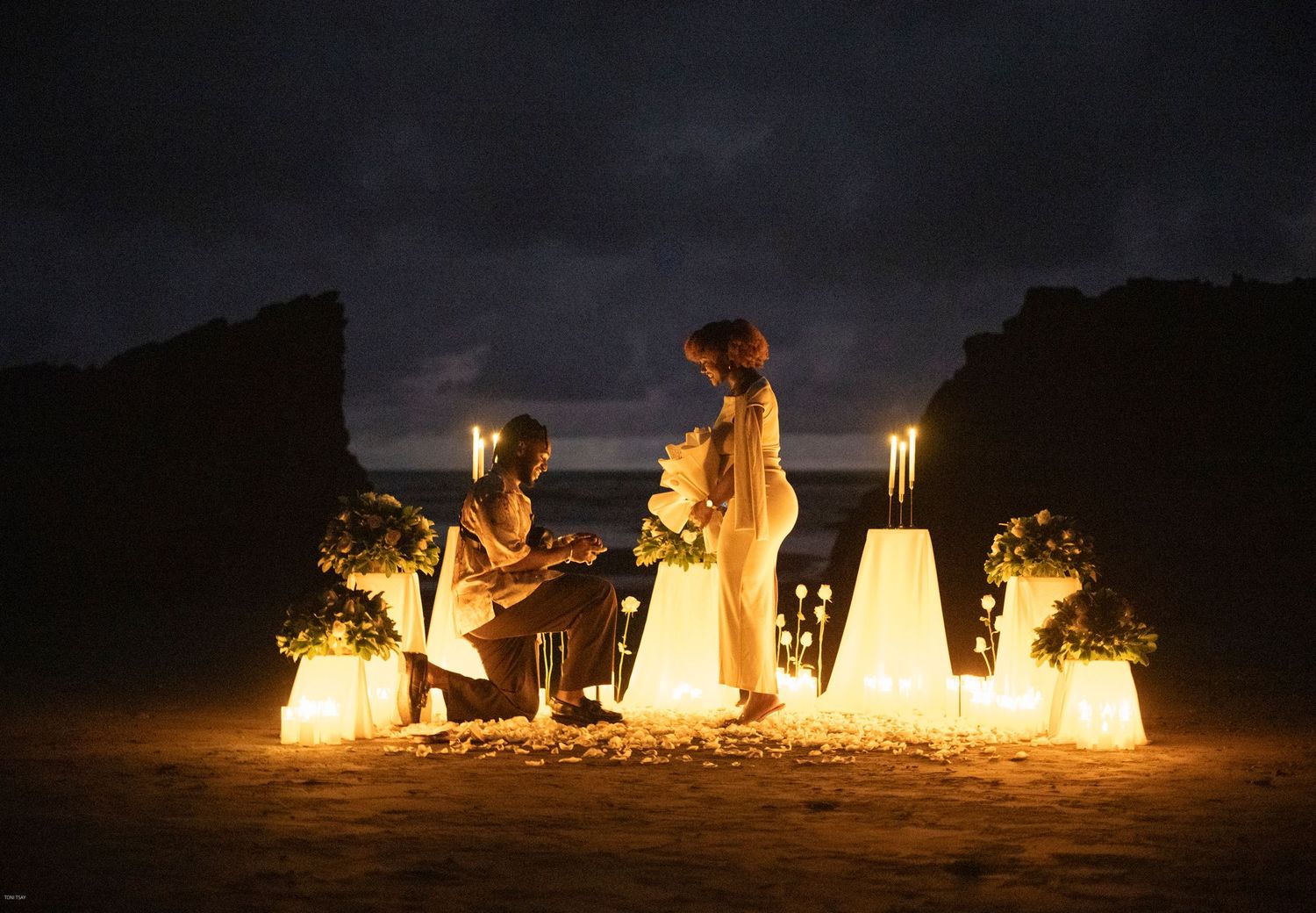 Illuminated white lanterns create a magical beach scene at night with silhouettes of people gathered around them.