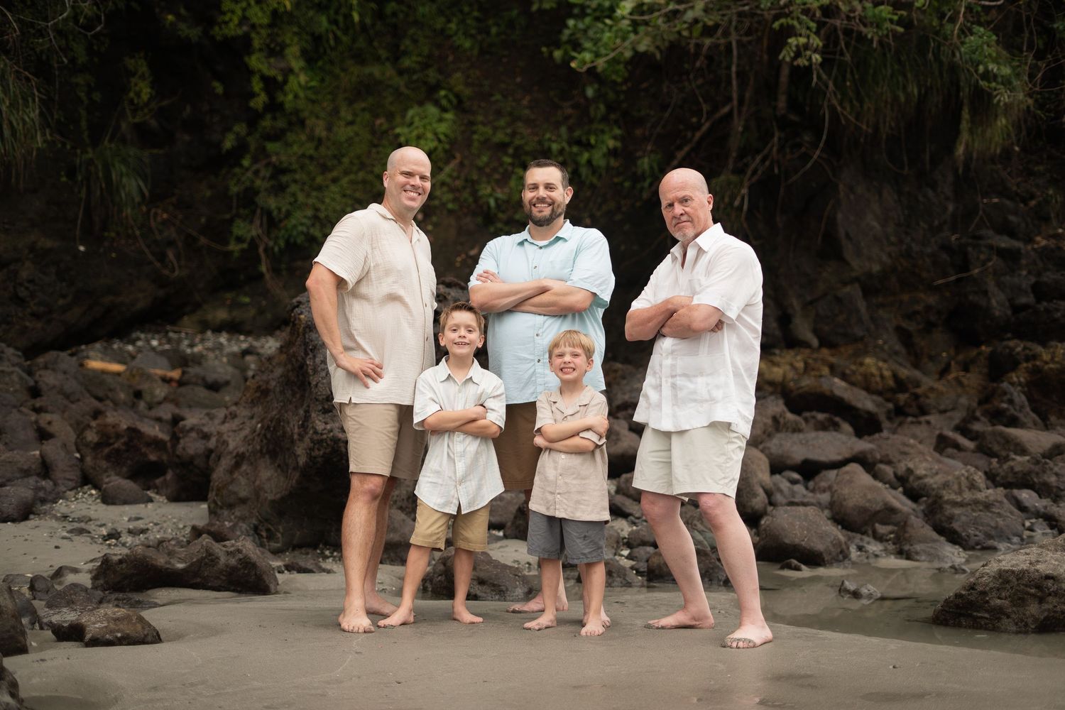 Family group wearing white casual clothes posing on black lava rocks at beach. Manuel Antonio, Costa Rica.