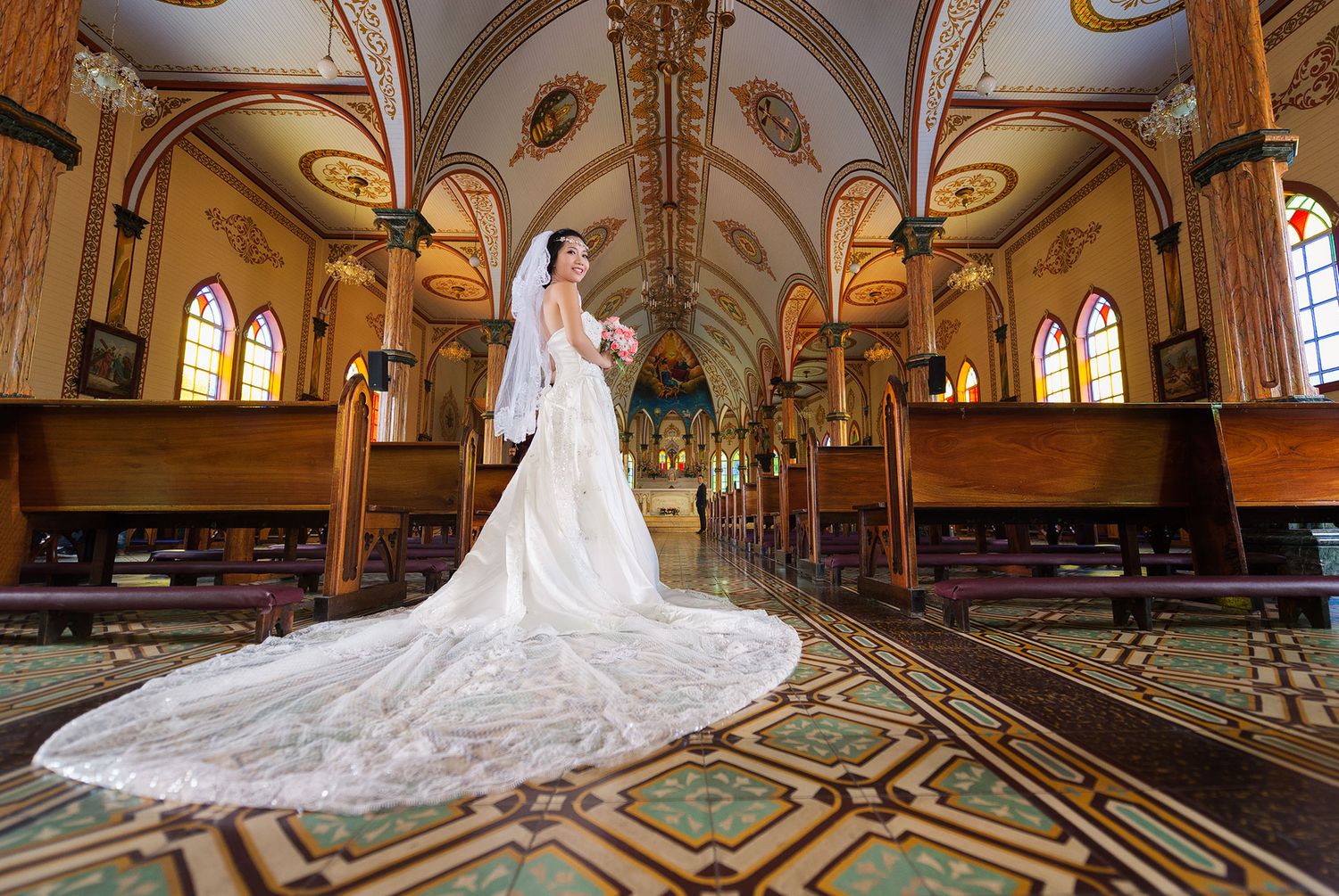 Ornate church interior with vaulted ceilings, stained glass windows and geometric floor patterns.