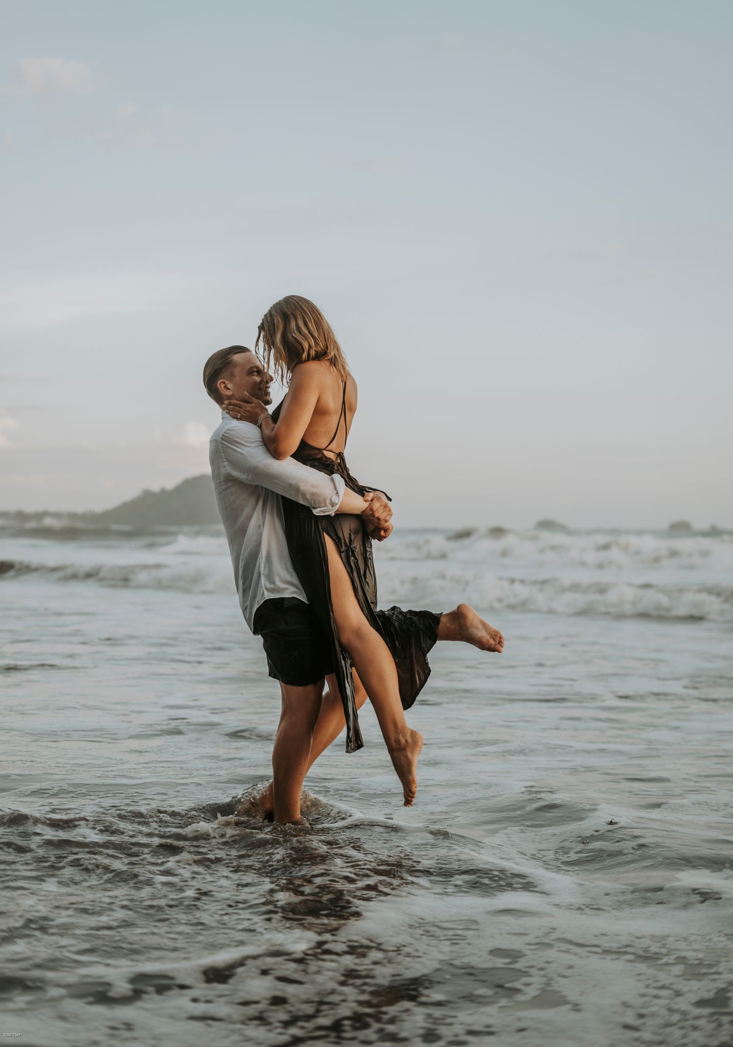 A couple embraces playfully in the ocean waves at sunset, creating a romantic and carefree seaside moment.